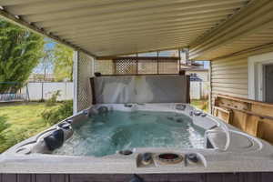 Covered outdoor spa area featuring a hot tub, slatted patio cover, and lattice privacy screen