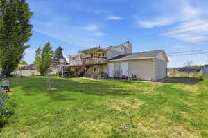 Expansive green lawn with a two-story residence featuring a second-story wooden deck, a ground-level covered patio, and an attached storage shed with two access doors