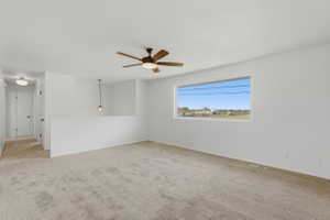 Spacious room featuring a large window, neutral carpeting, and a ceiling fan with integrated lighting