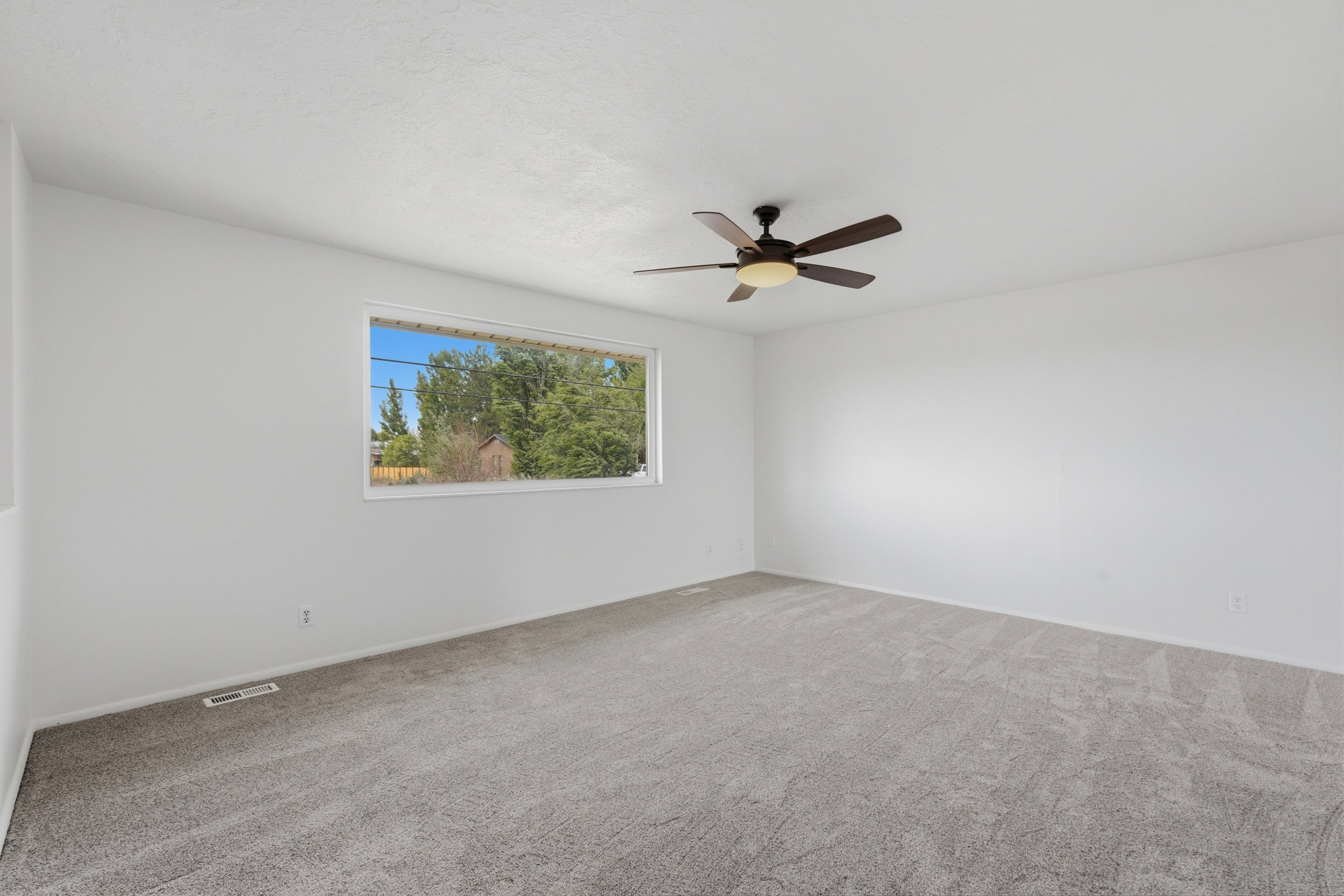 Spacious room with light gray carpeting, neutral white walls, and a large window