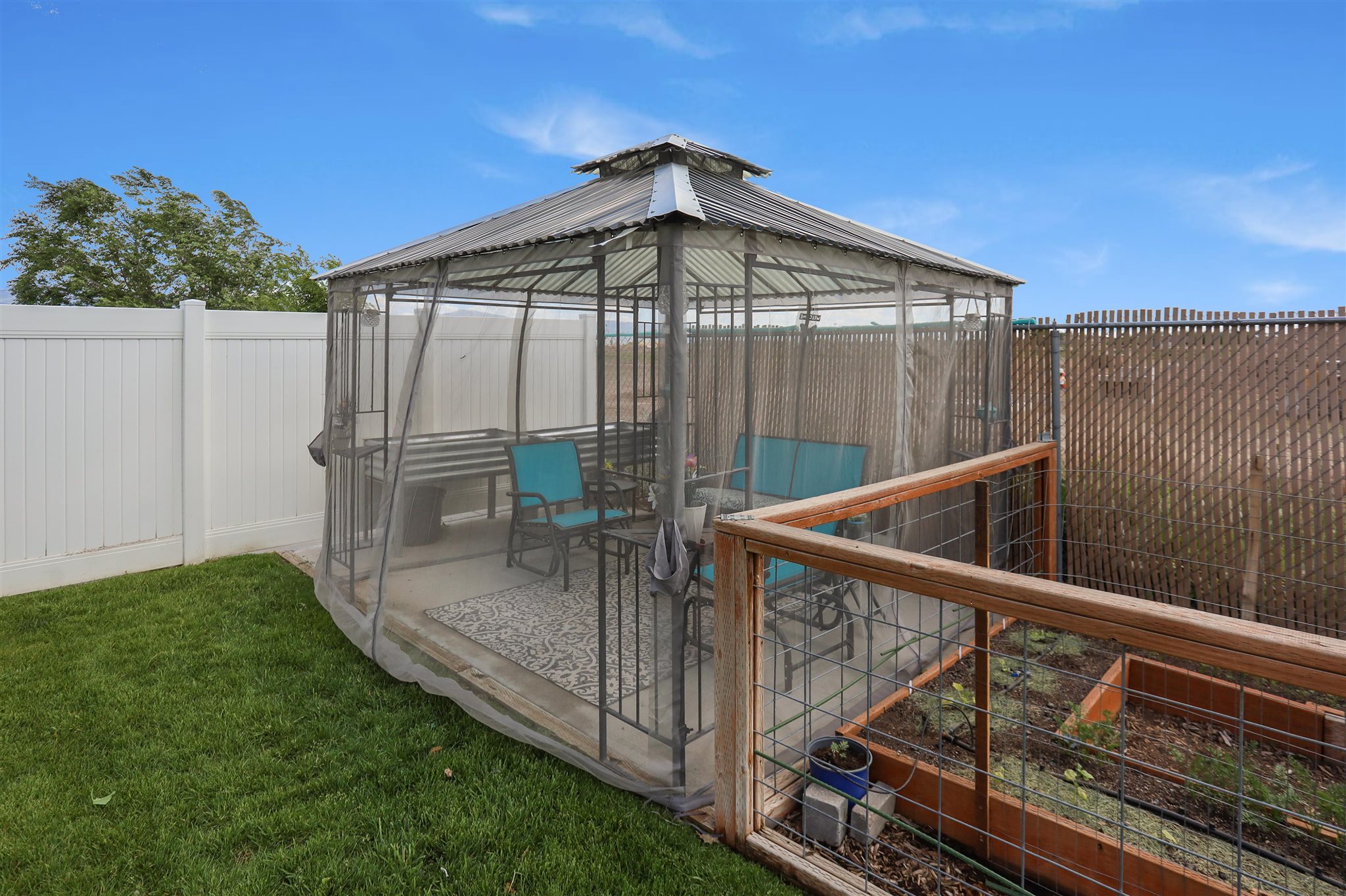 Screened gazebo with a corrugated metal roof, concrete patio base, and surrounding manicured lawn