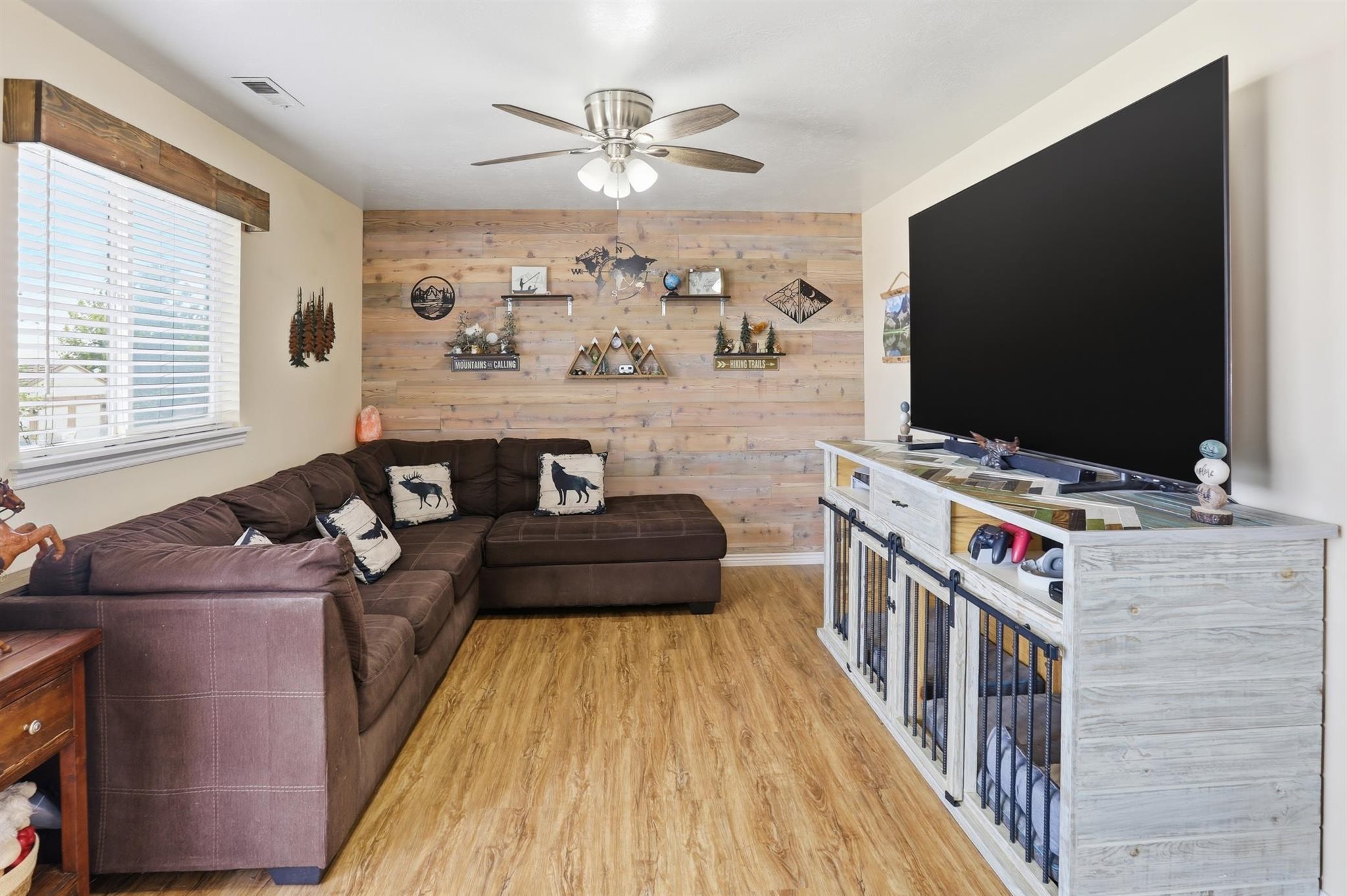 Famiiy room featuring plank wood-finish flooring, a decorative accent wall, and a ceiling fan with integrated lighting