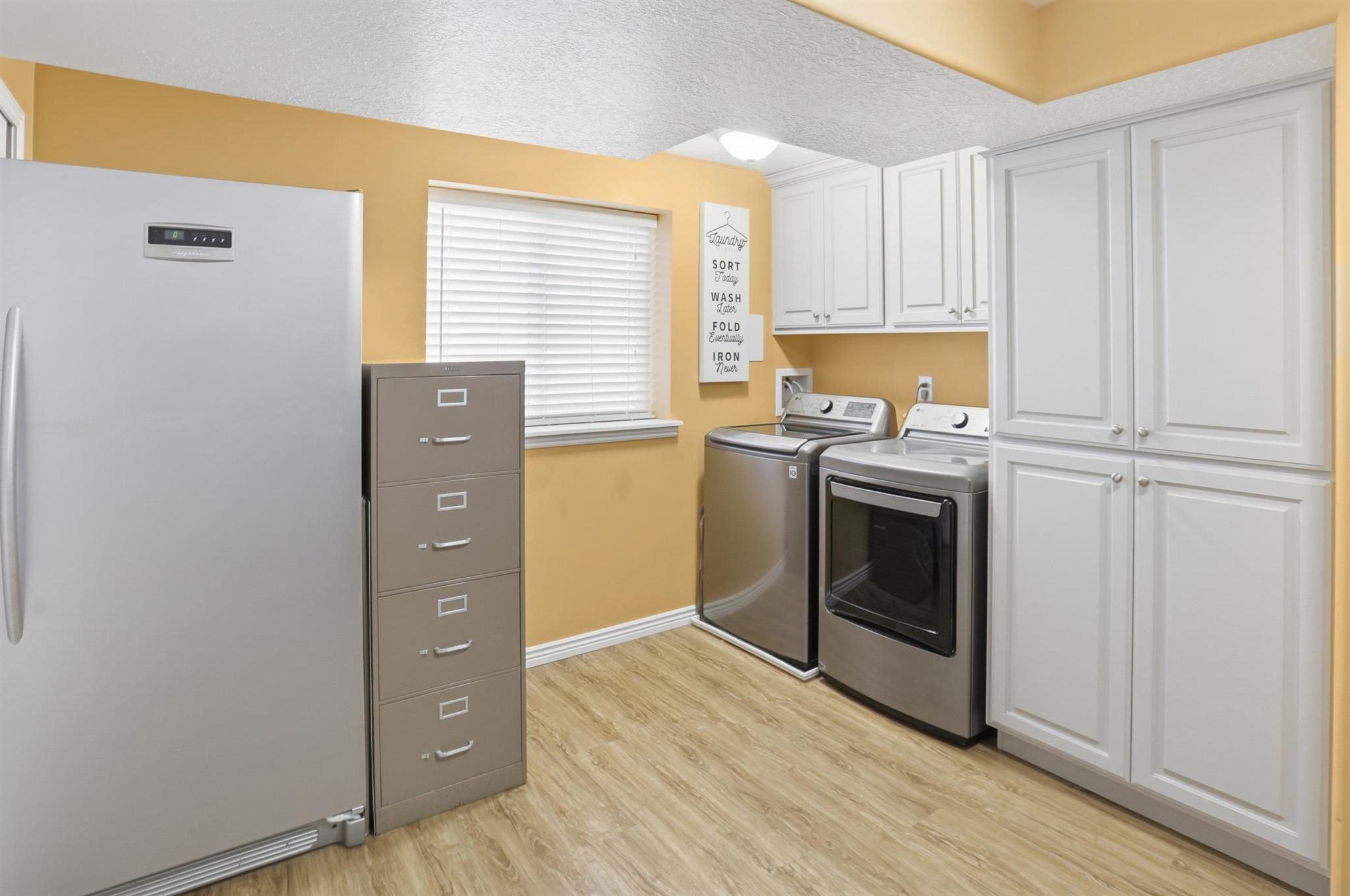 Dedicated laundry space featuring wood-finish flooring, white cabinetry, and a bright window