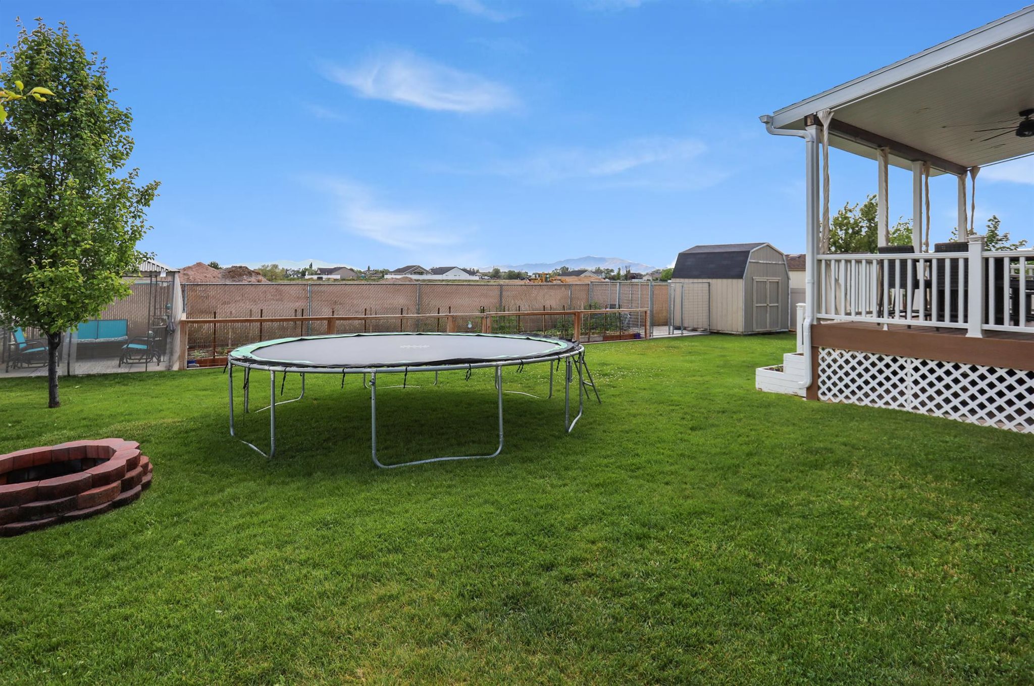 Expansive backyard featuring a manicured lawn, a red brick fire pit, and a covered back patio with white railings. Fully fenced