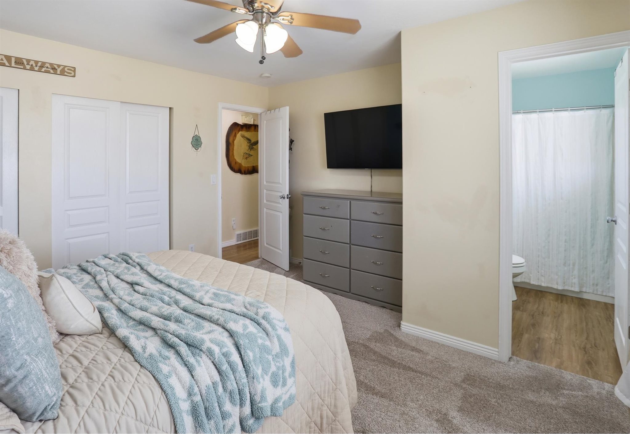 Primary Bedroom with direct bathroom access, featuring a ceiling fan with integrated lighting, bi-fold closet doors, and wood-finish flooring in the bathroom and new carpet