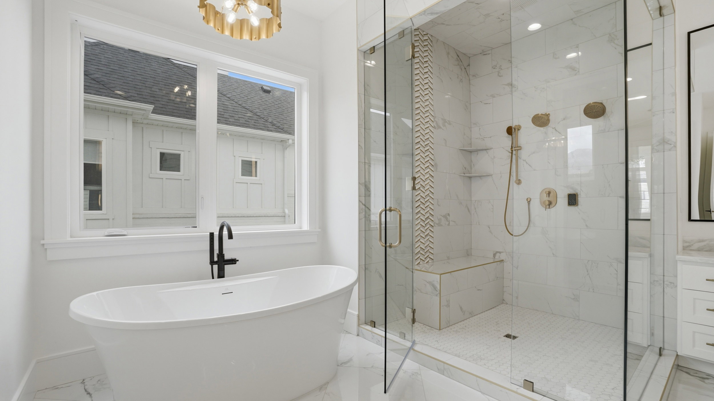 Freestanding soaking tub with a matte black faucet, full glass shower enclosure with a built-in bench, marble-finish tile, and brass shower fixtures