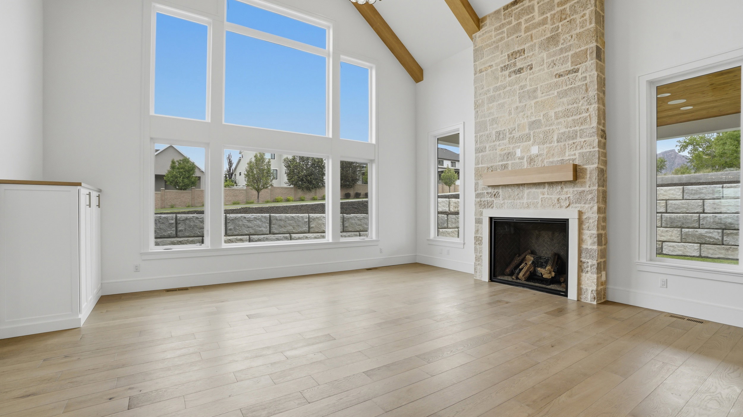 Vaulted living space featuring a floor-to-ceiling stone fireplace with a wood mantle, wood-finish flooring, exposed ceiling beams, and a built-in cabinet with a wood countertop