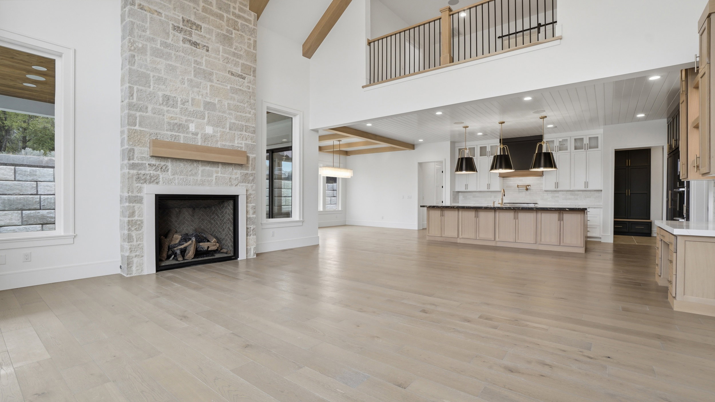 Spacious living area featuring a stone fireplace, wood-finish flooring, and high ceilings with exposed beams