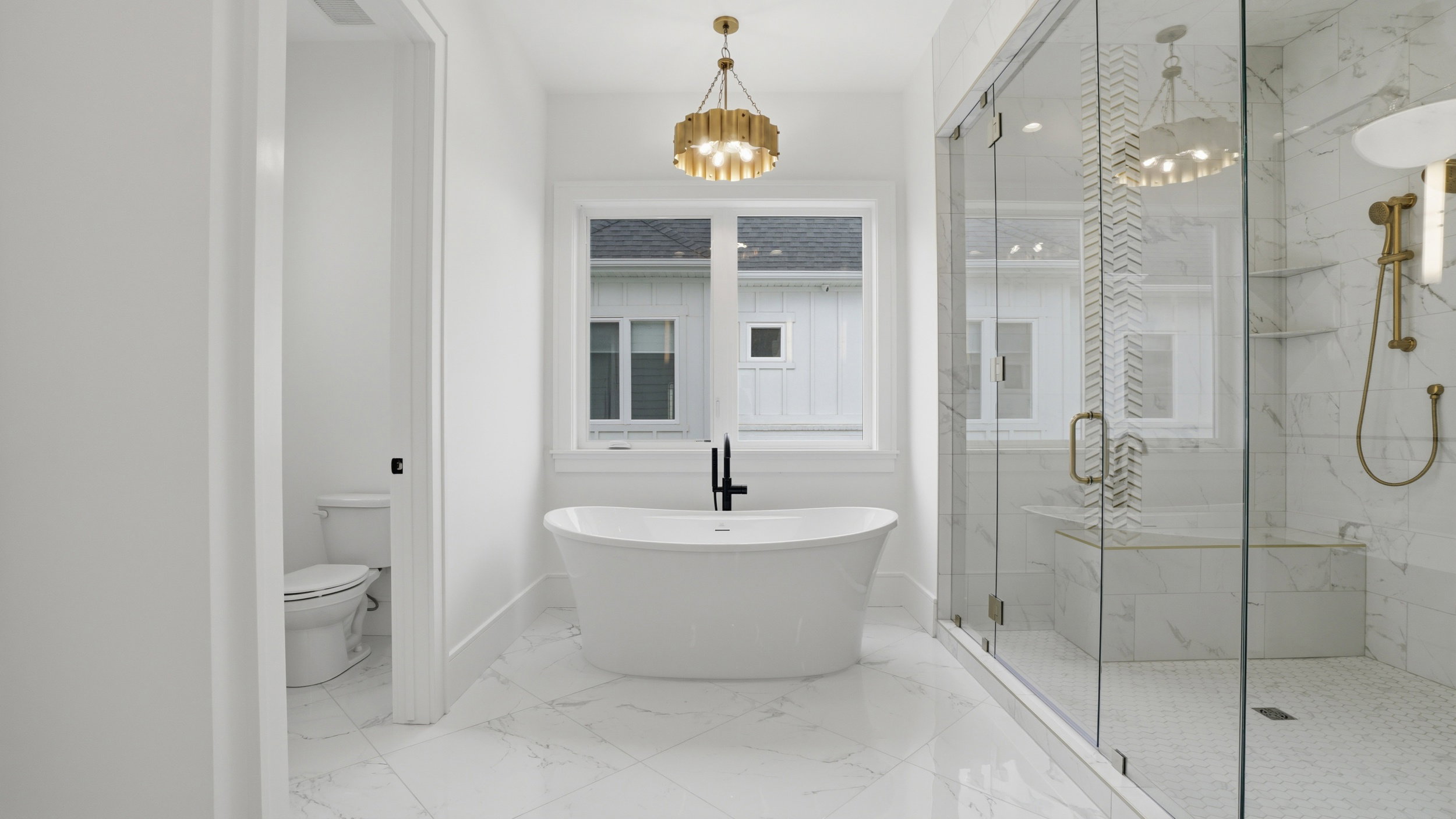 Freestanding bathtub with a black wall-mounted faucet, complemented by a gold-finish chandelier