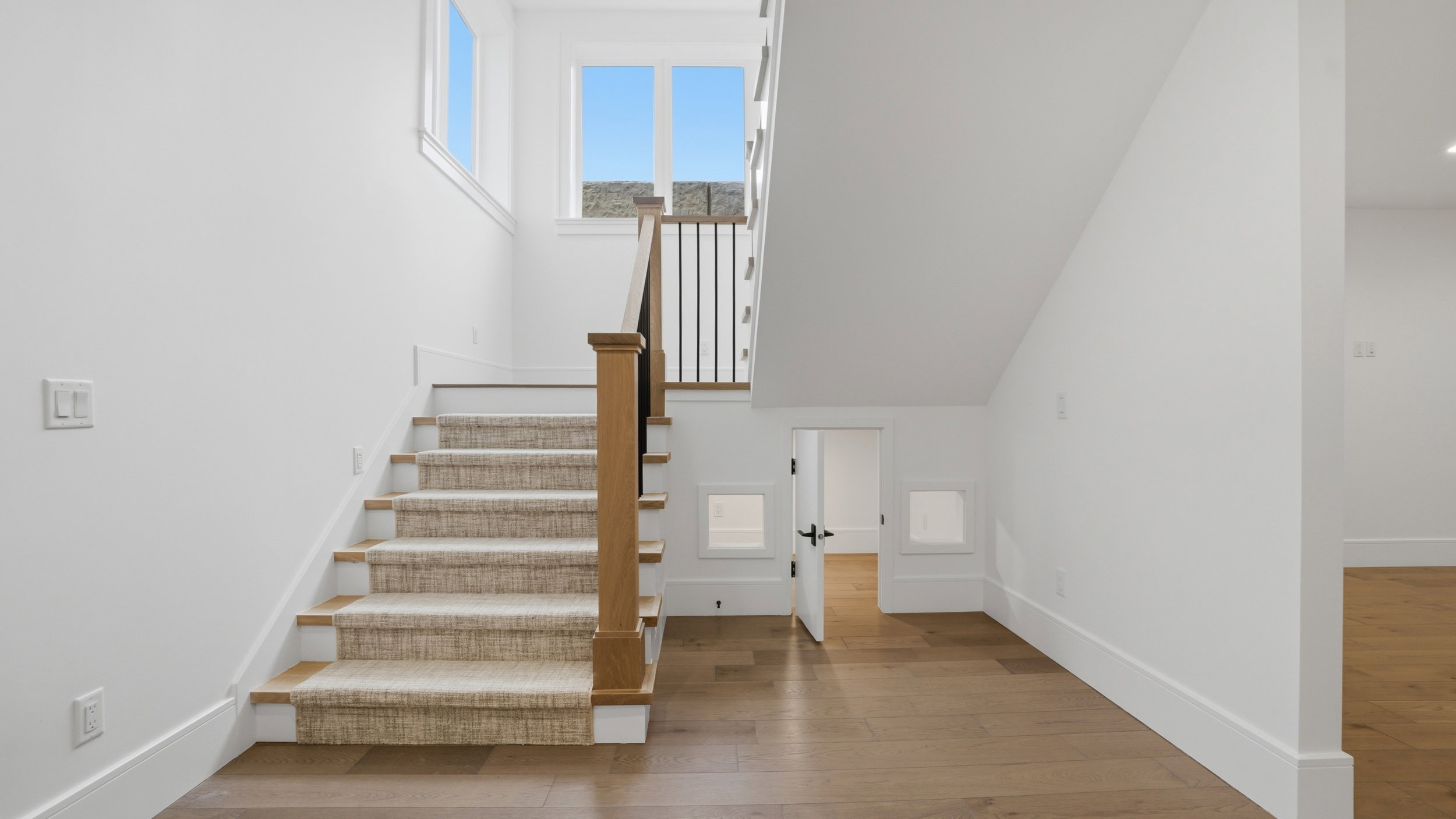 Staircase featuring wood-finish treads and a neutral-toned runner, complemented by a wood-finish newel post and black metal balusters
