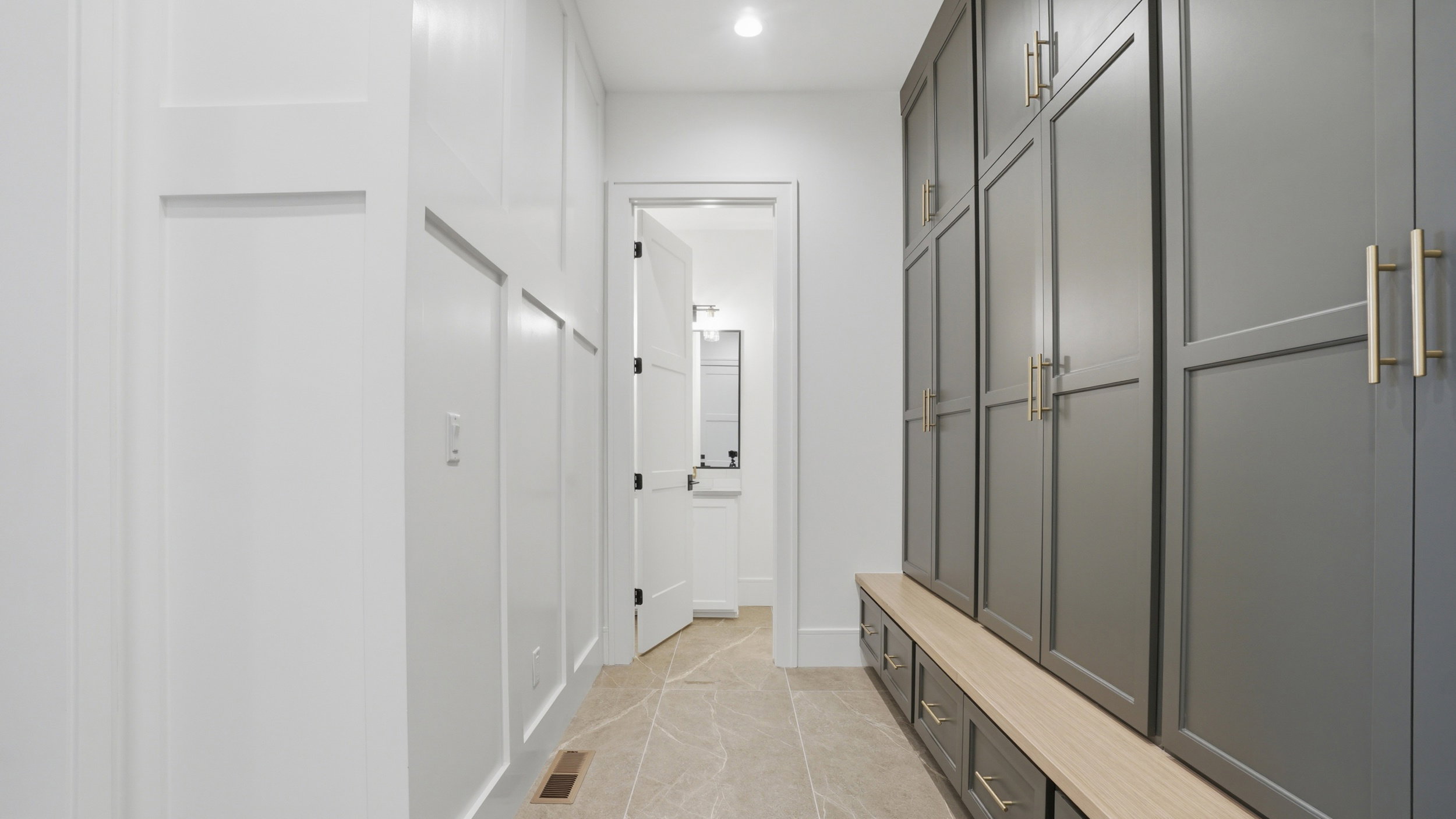 Hallway featuring board-and-batten wall detailing, large format tile flooring, built-in cabinetry with gold-toned hardware, and an integrated bench with storage drawers