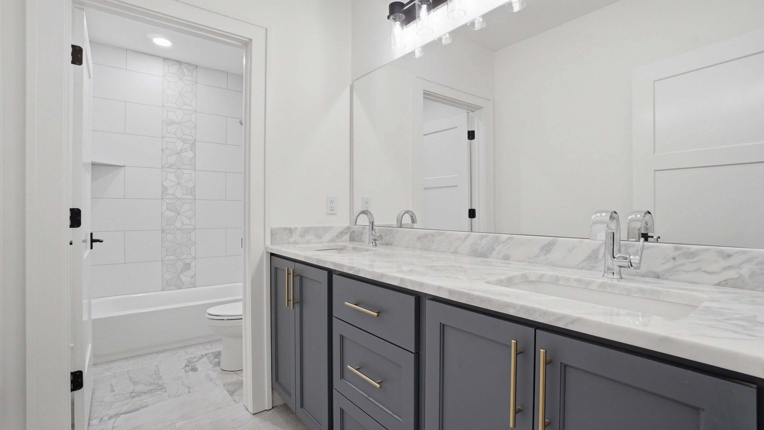 Double vanity with marble-finish countertop and integrated sinks, featuring gray cabinetry with gold-tone hardware