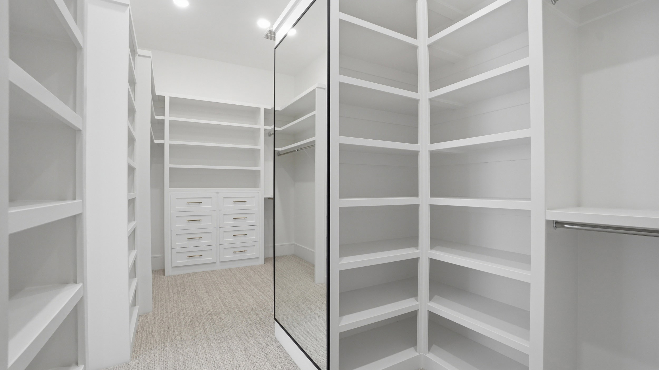 Custom closet system featuring extensive shelving, built-in drawers with modern hardware, and a full-length mirrored door