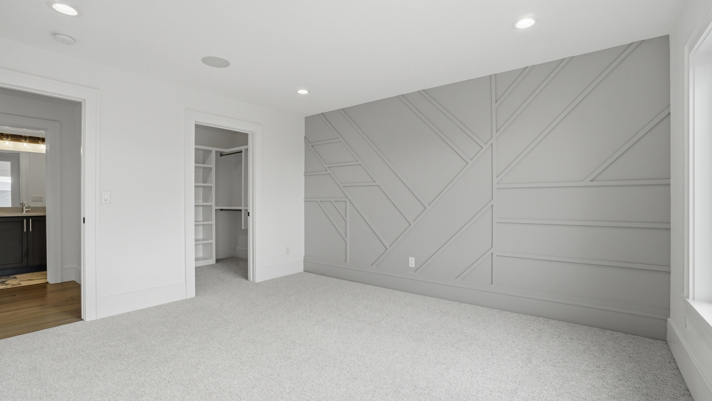 Room featuring a statement wall with geometric paneling, light-toned carpeting, recessed ceiling lighting, and a walk-in closet with built-in shelving