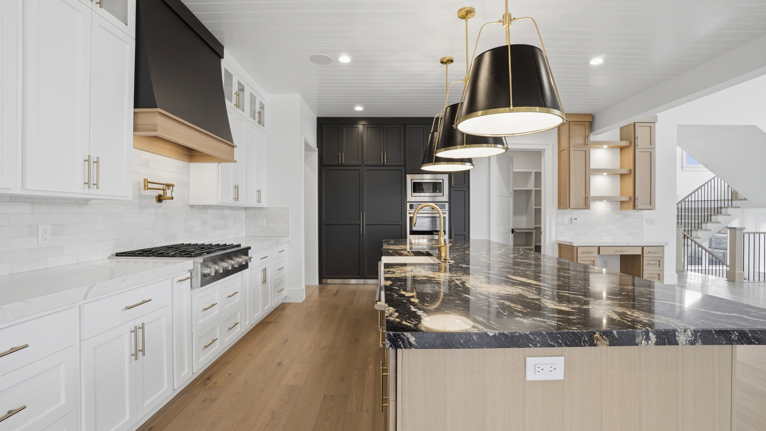 Kitchen featuring a large island with a patterned countertop, white perimeter cabinetry, a stainless steel range with a pot filler faucet, and wood-finish flooring