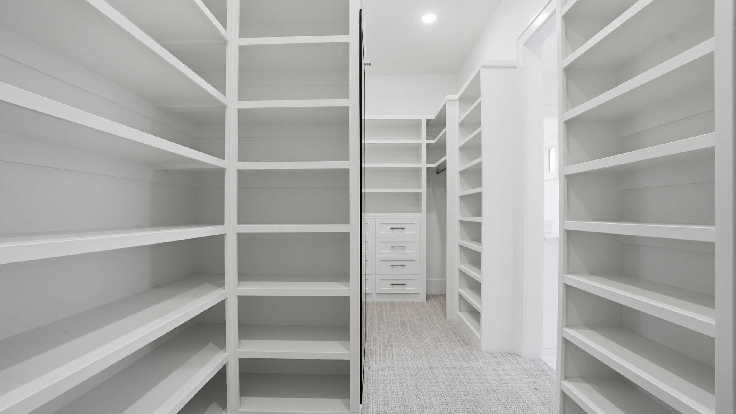 Expansive walk-in closet featuring built-in shelving, integrated drawer storage, a hanging rod, recessed lighting, and light-toned flooring