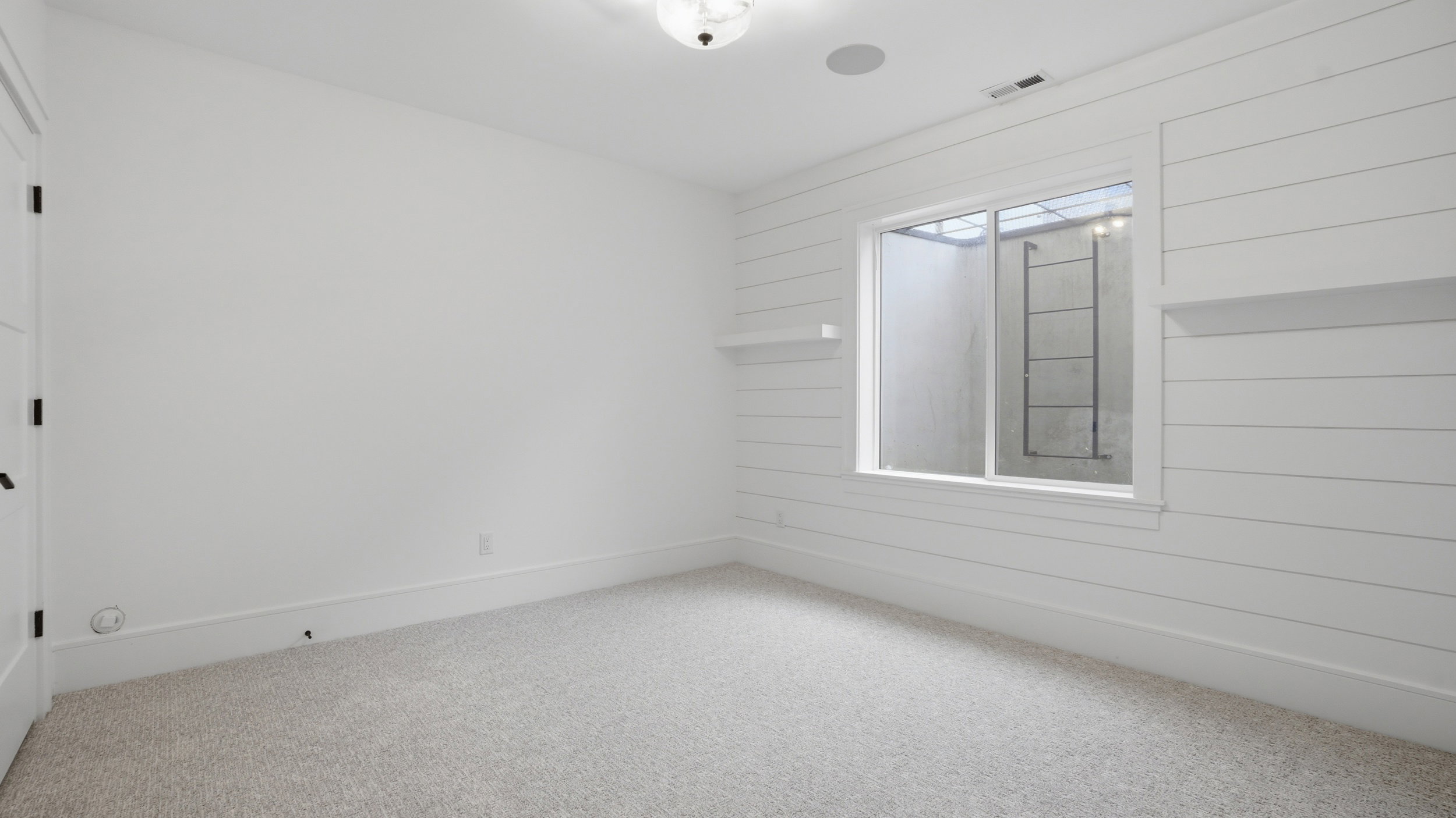 Room featuring shiplap accent wall with integrated shelving, window with exterior ladder, recessed ceiling speaker, and light-toned carpet flooring