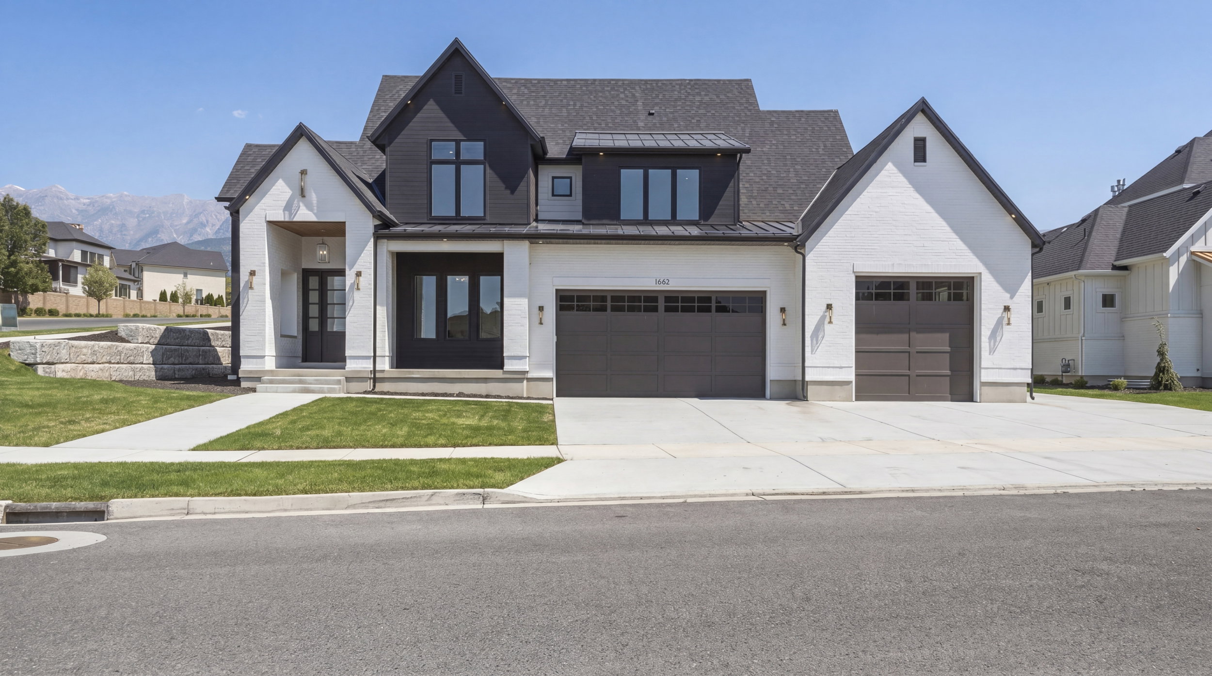 Modern farmhouse exterior featuring a black and white facade, a two-car garage, an additional single-car garage, a covered entryway, and mountain scenery