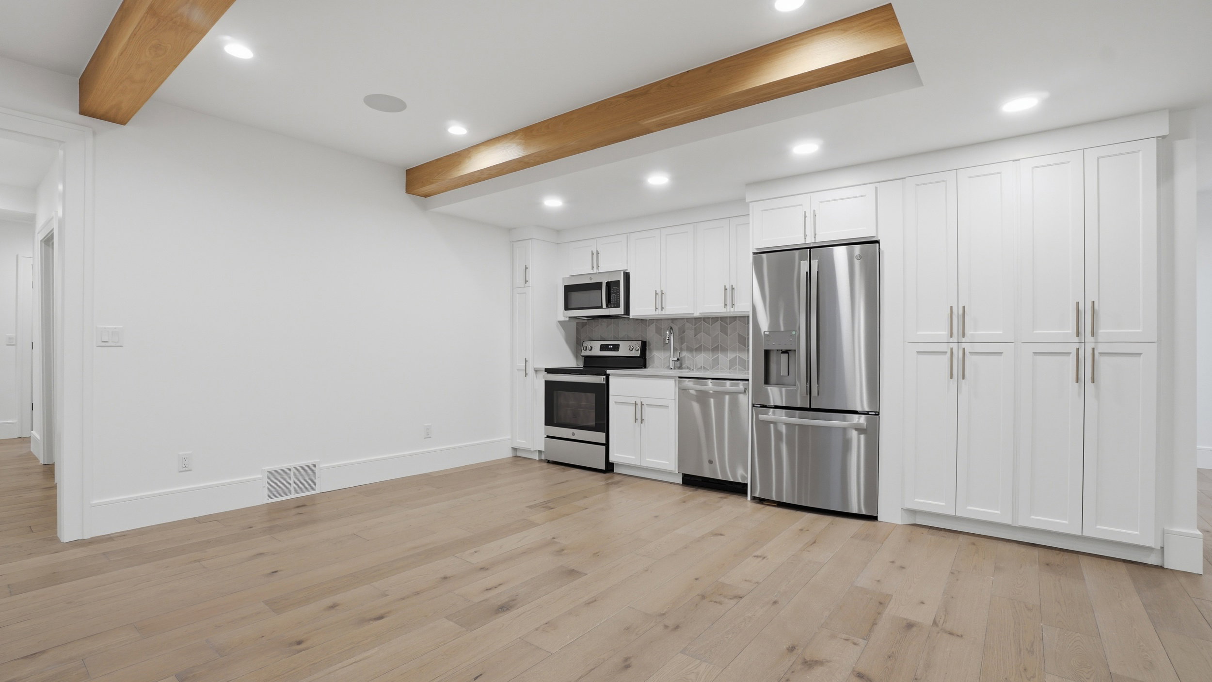 Bright kitchen area featuring white cabinetry, stainless steel appliances, wood-finish flooring, recessed lighting, and exposed ceiling beams