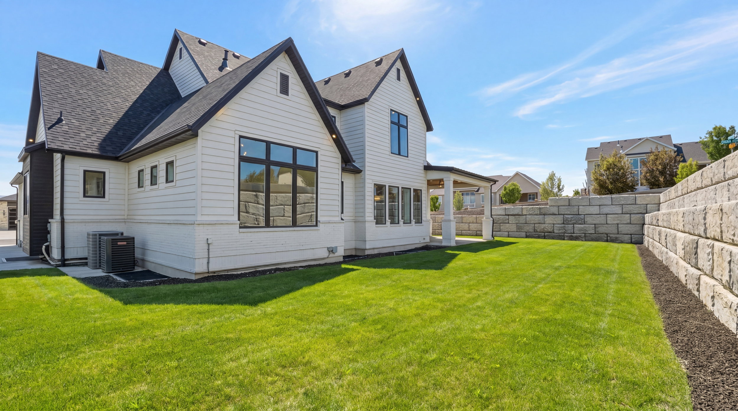 Spacious backyard featuring a manicured lawn, a large retaining wall, and a covered patio area with white columns