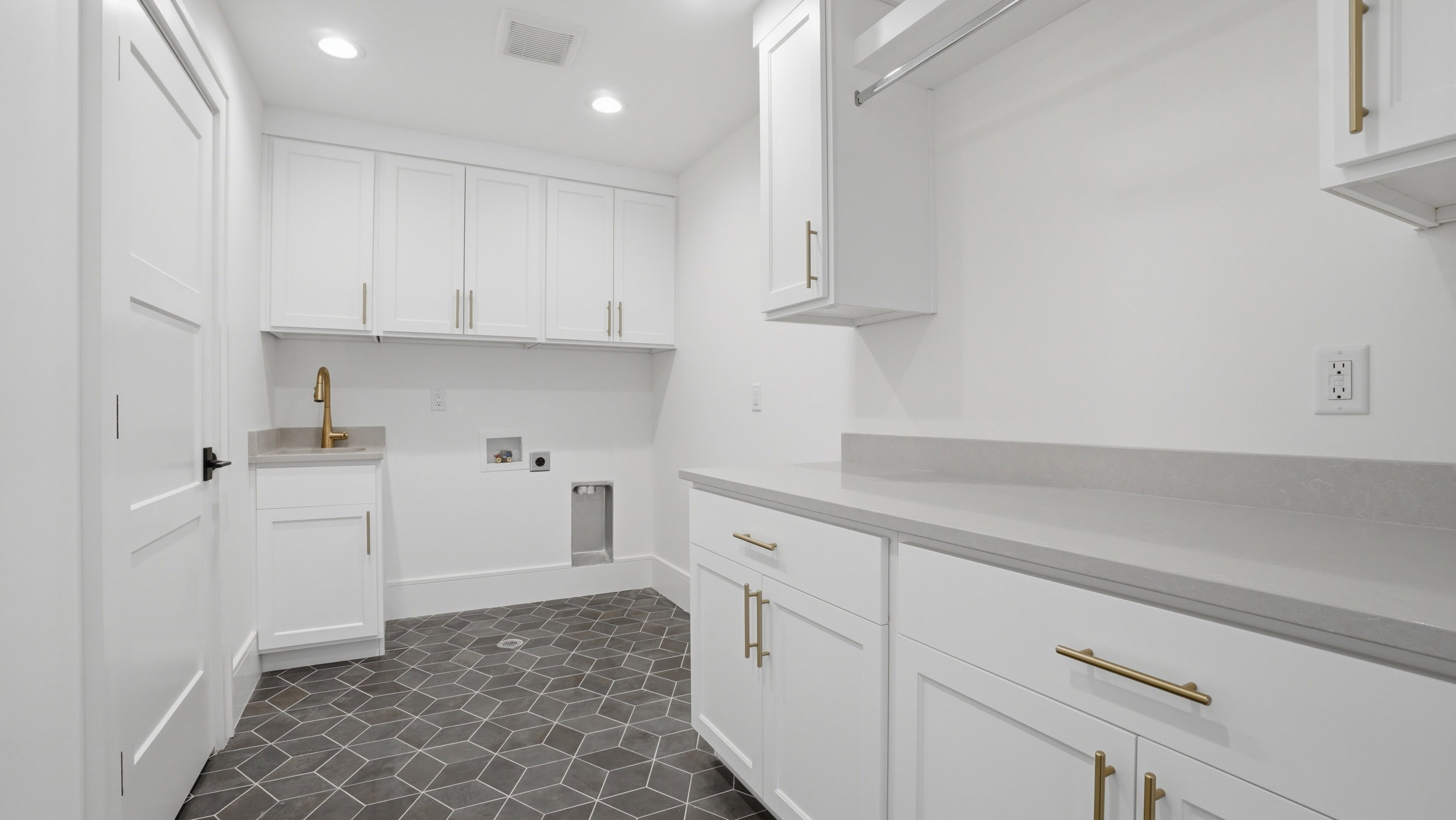 Dedicated laundry space featuring white shaker cabinetry, an integrated sink with a gold-finish faucet, and substantial countertop space