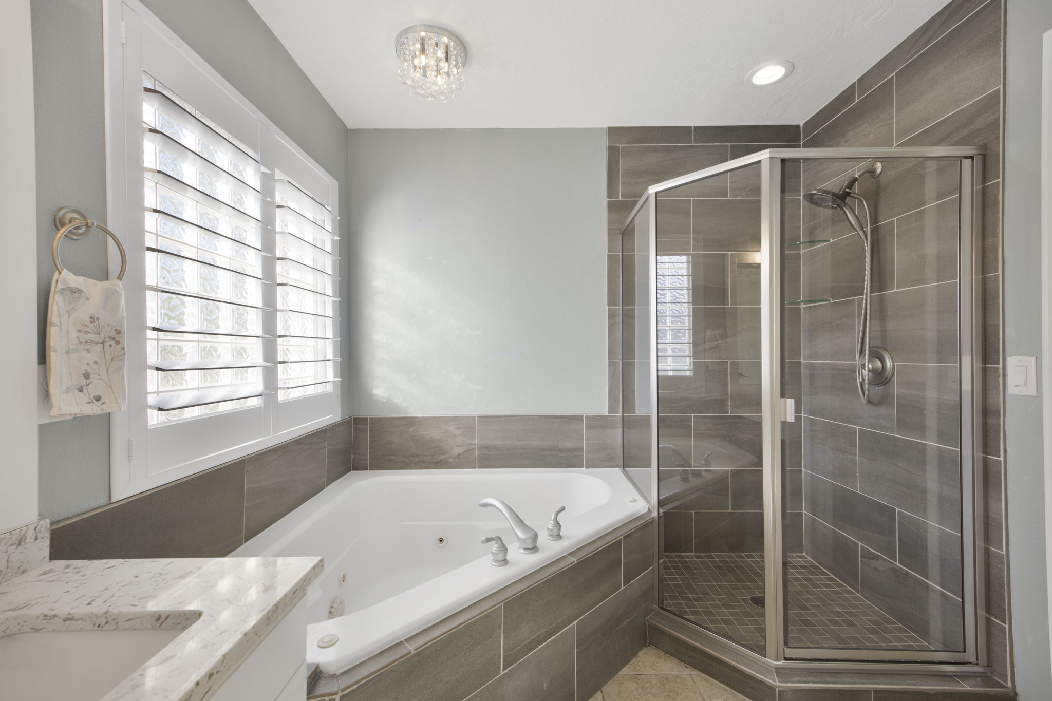Bathroom featuring a corner soaking tub, walk-in shower with glass enclosure, tiled walls, plantation shutters, and a crystal flush mount light fixture