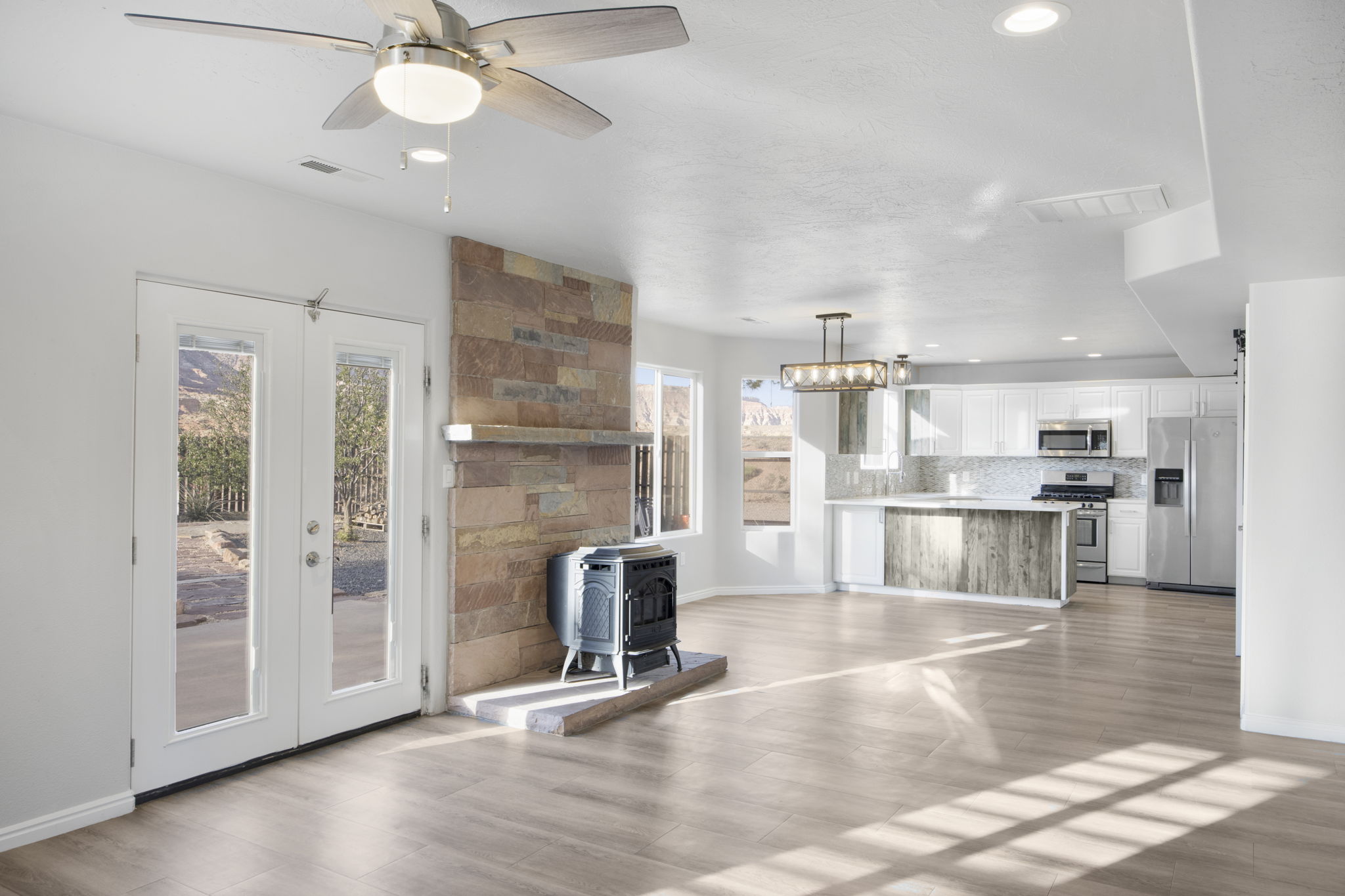 Open-concept living area featuring wood-finish flooring, a stone-stacked fireplace with a wood mantle, and white double French doors