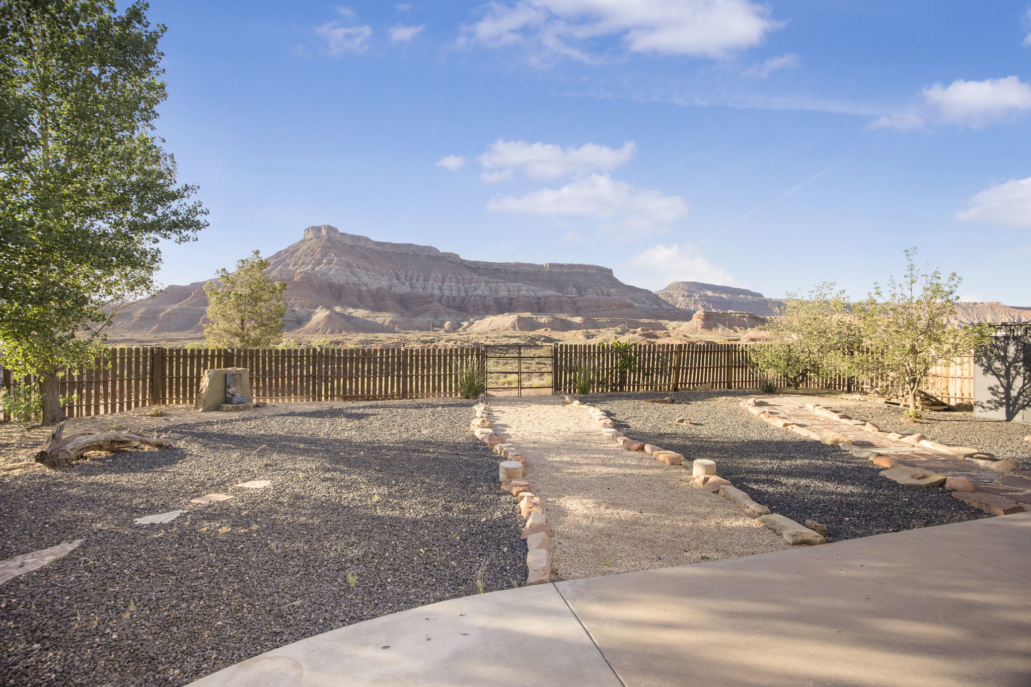 Expansive desert landscaping featuring gravel and stone pathways, a wood-slat perimeter fence, and a distant mountain backdrop