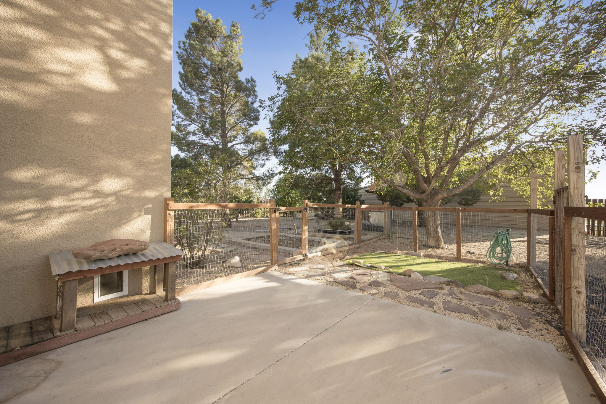 Outdoor patio area featuring a concrete surface, fenced perimeter, mature trees, and a gravel and stone landscape