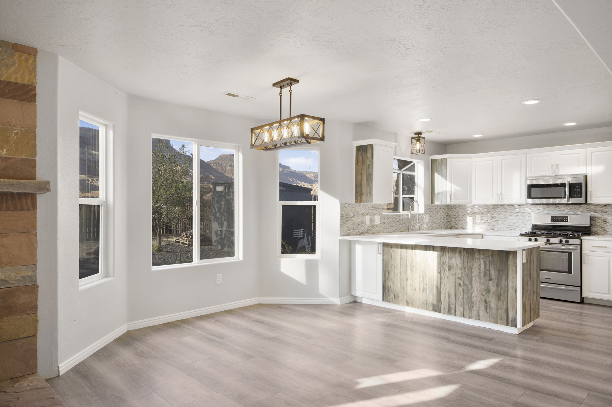 Open-concept living space featuring wood-finish flooring, a stone-faced fireplace, and expansive windows