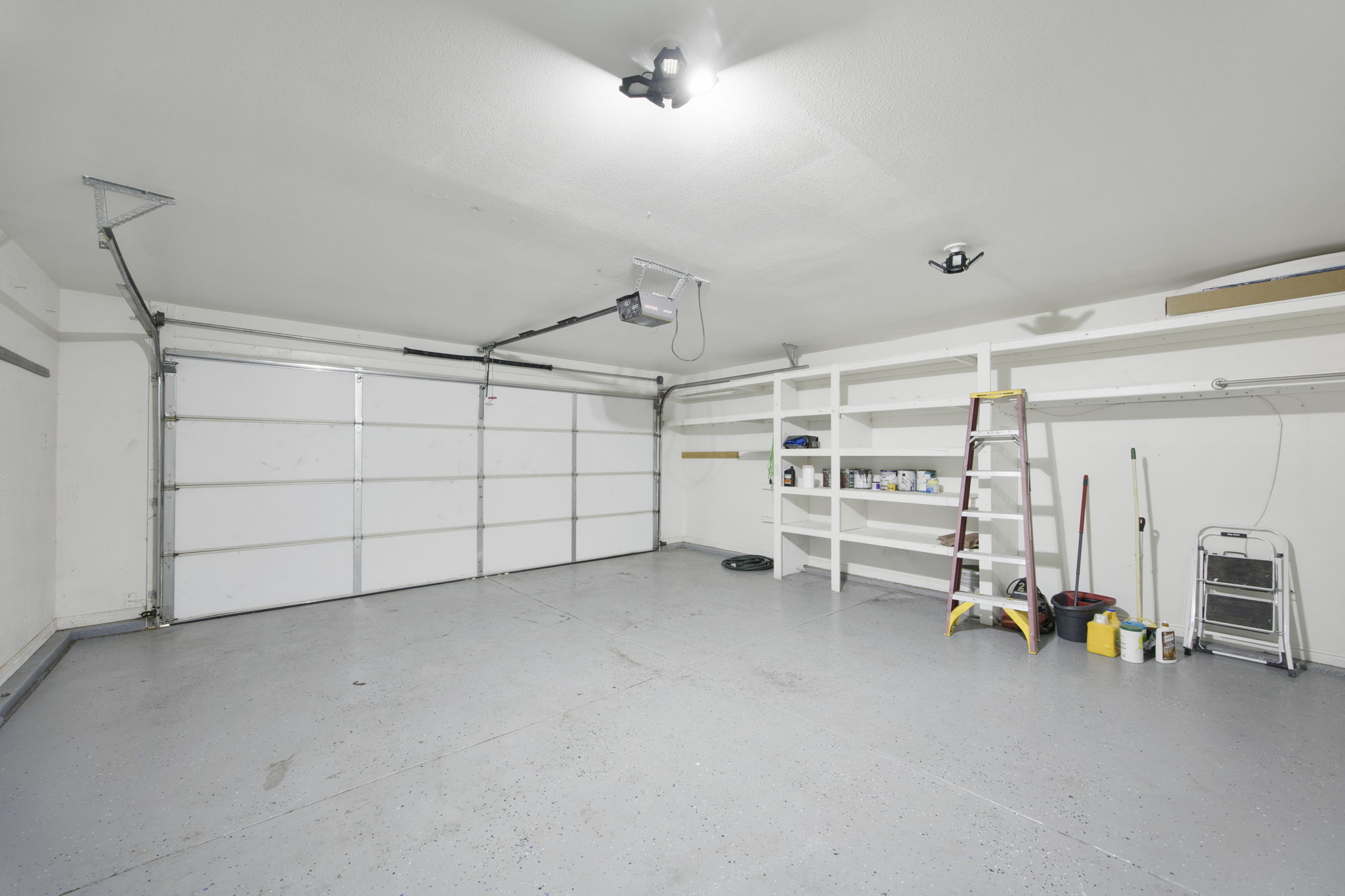 Spacious garage featuring two overhead doors, built-in shelving, and a speckled epoxy floor finish