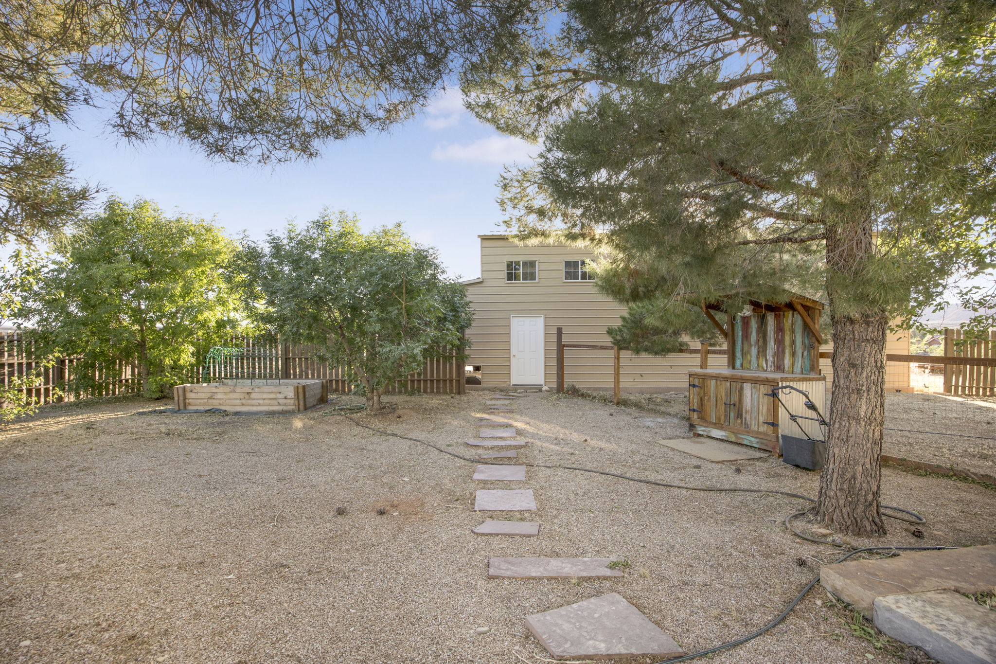 Expansive gravel yard featuring mature trees and a fenced perimeter