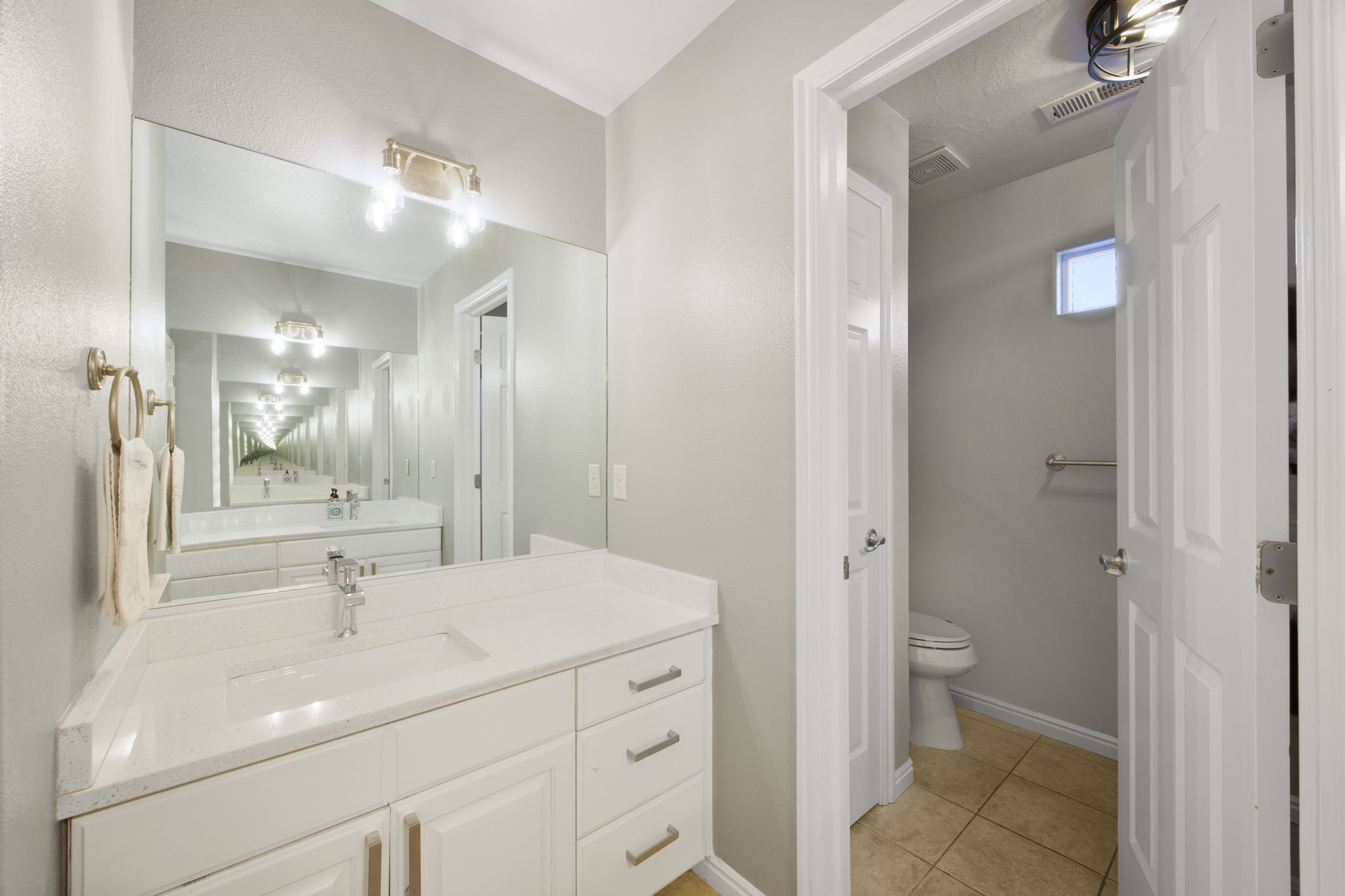 Bathroom vanity featuring a light-toned countertop, integrated sink, and white cabinetry with brushed gold hardware