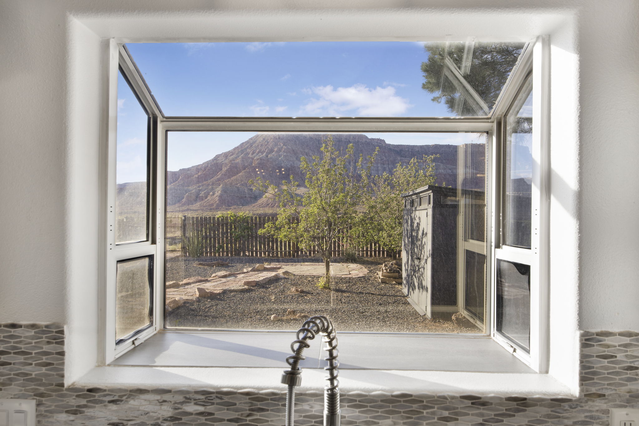 Expansive kitchen window featuring a mountain backdrop, a fenced yard, and a pull-down faucet