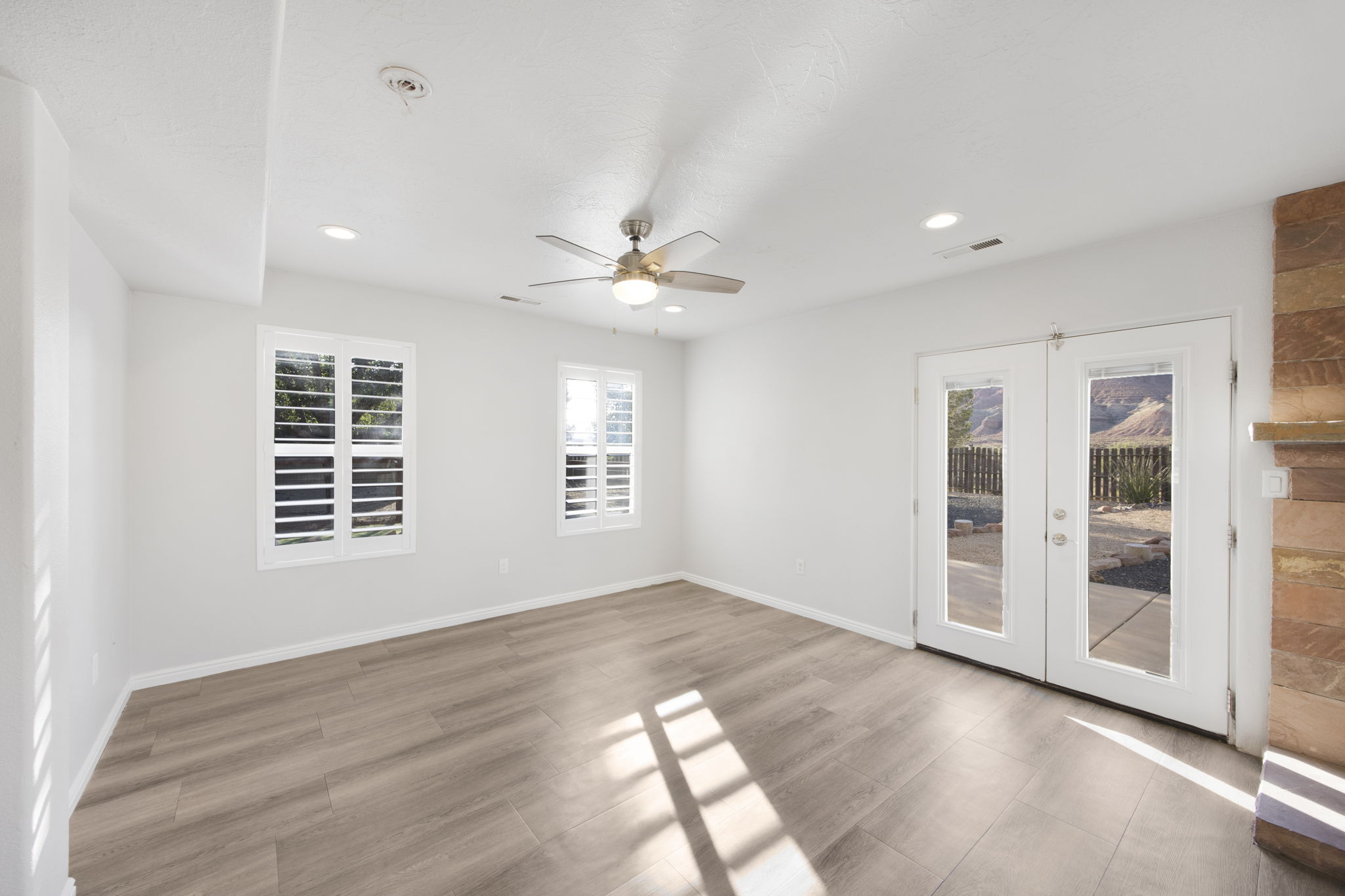 Spacious room featuring wood-finish flooring, two windows with plantation shutters, recessed lighting, and a ceiling fan
