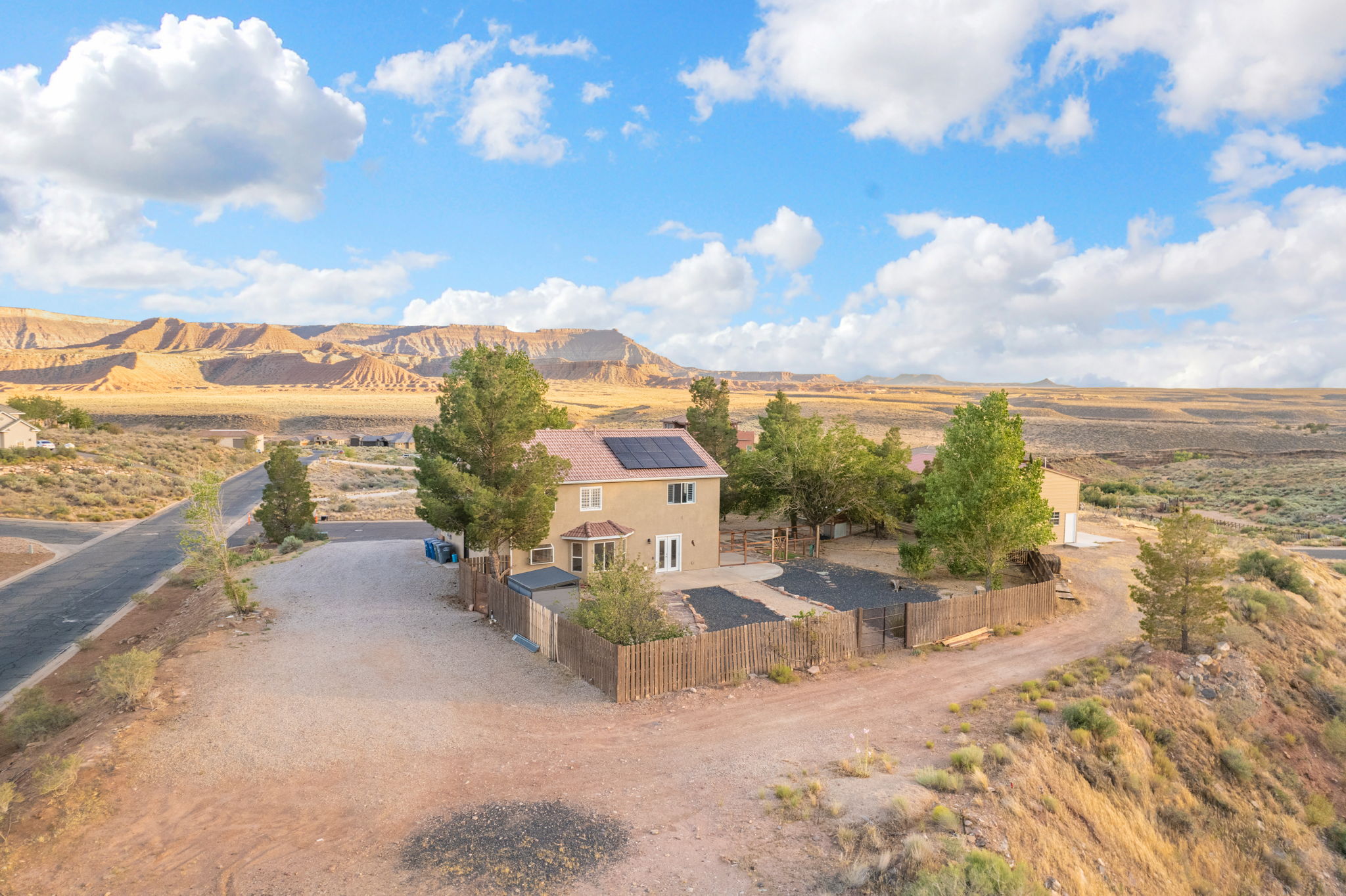 Two-story stucco residence featuring a fenced backyard, mature trees, and solar panels on the roof