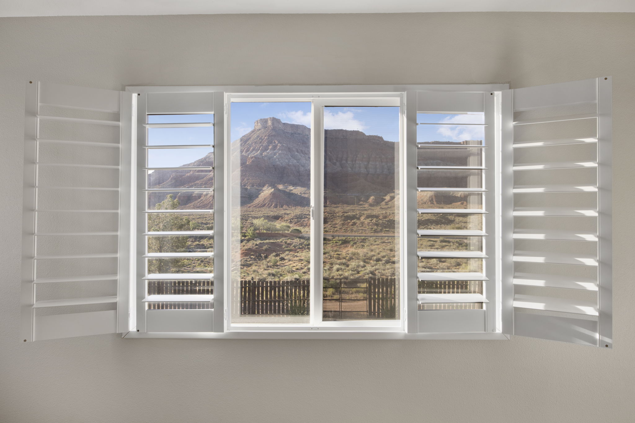Window with white plantation shutters, offering expansive mountain scenery