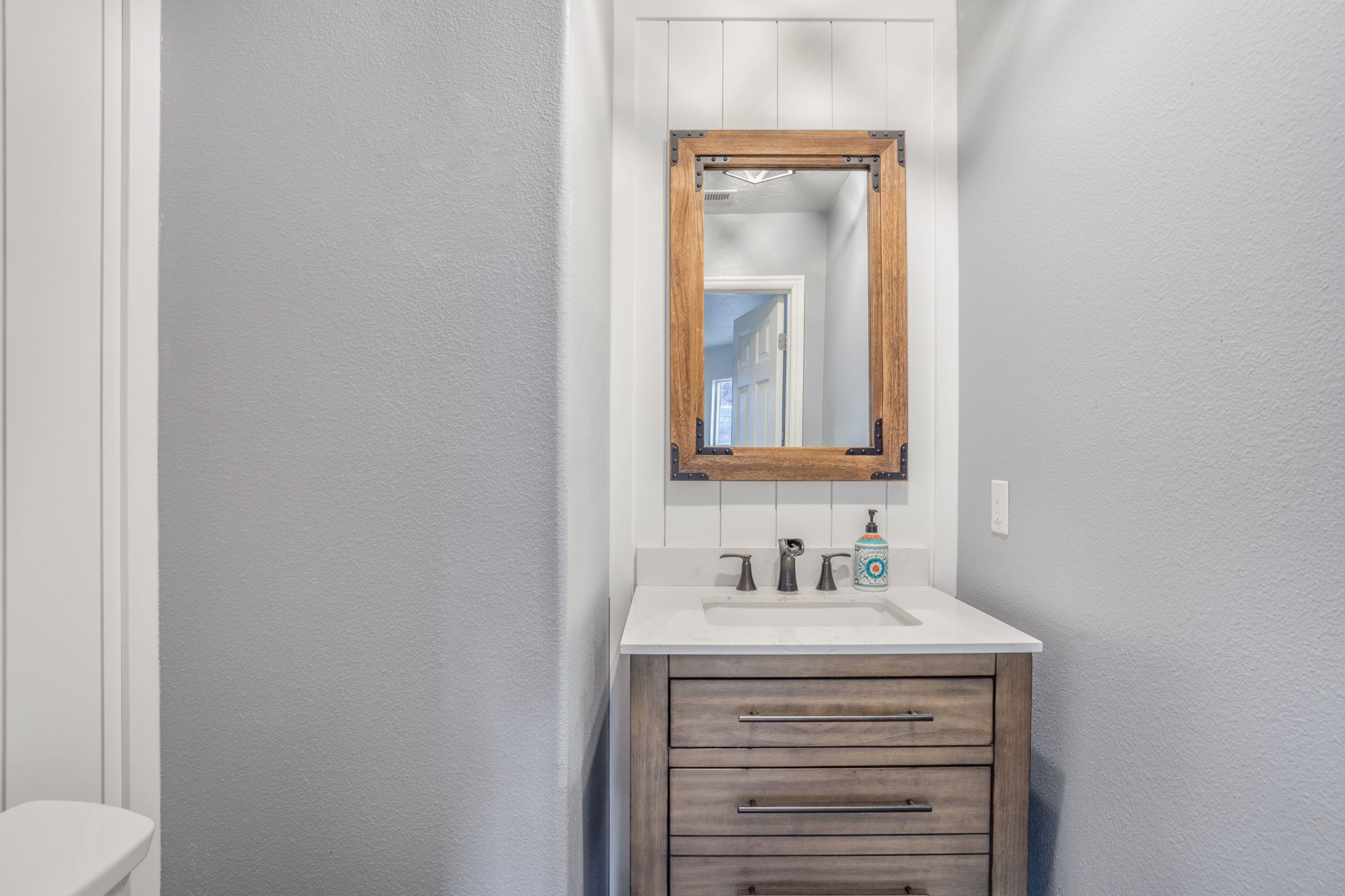 Powder room featuring a wood-finish vanity with drawer storage, white countertop, rectangular undermount sink, and dark bronze-finish faucet