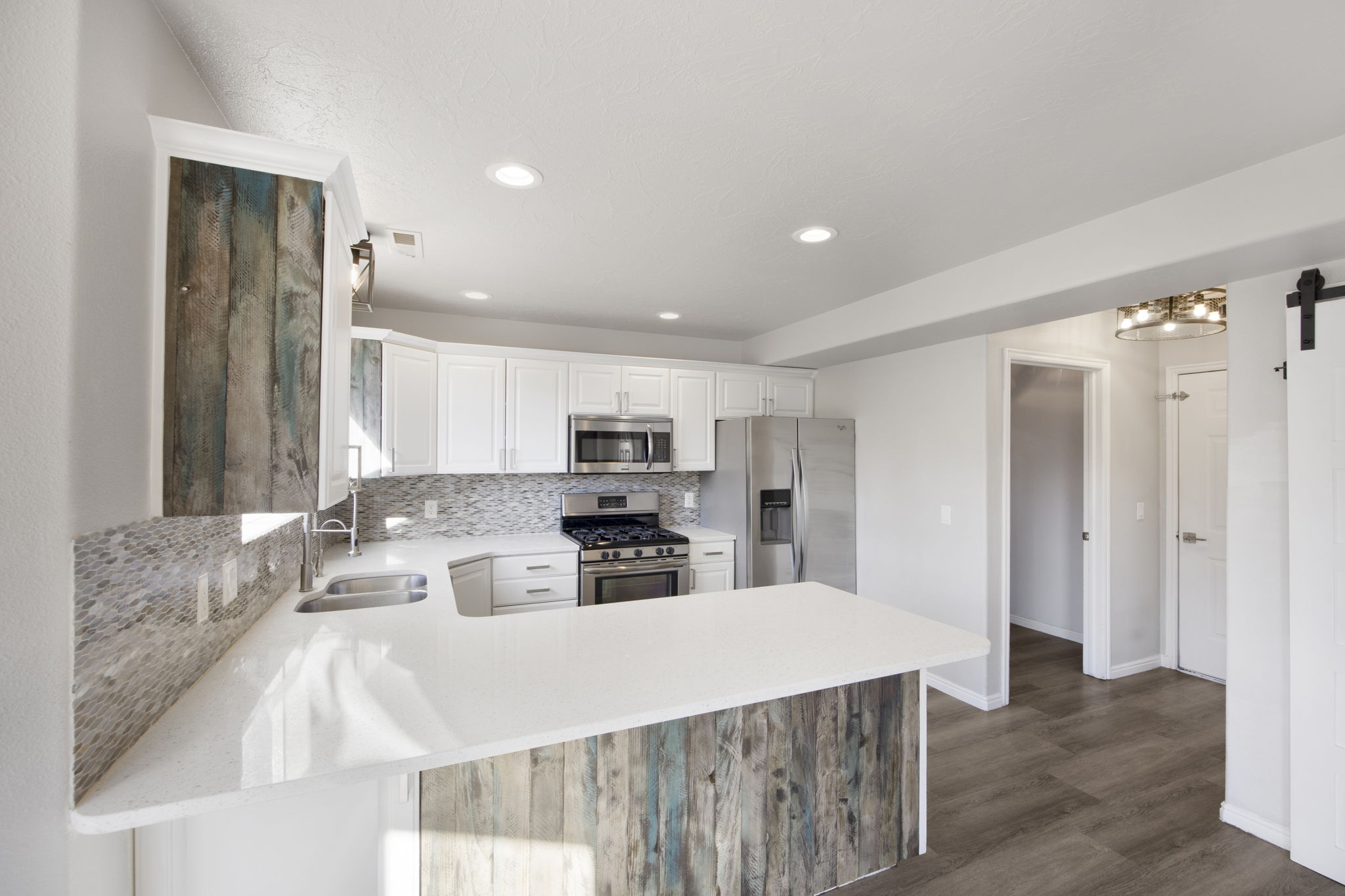 Kitchen featuring white cabinetry, stainless steel appliances, a tile backsplash, light countertops, and wood-finish flooring