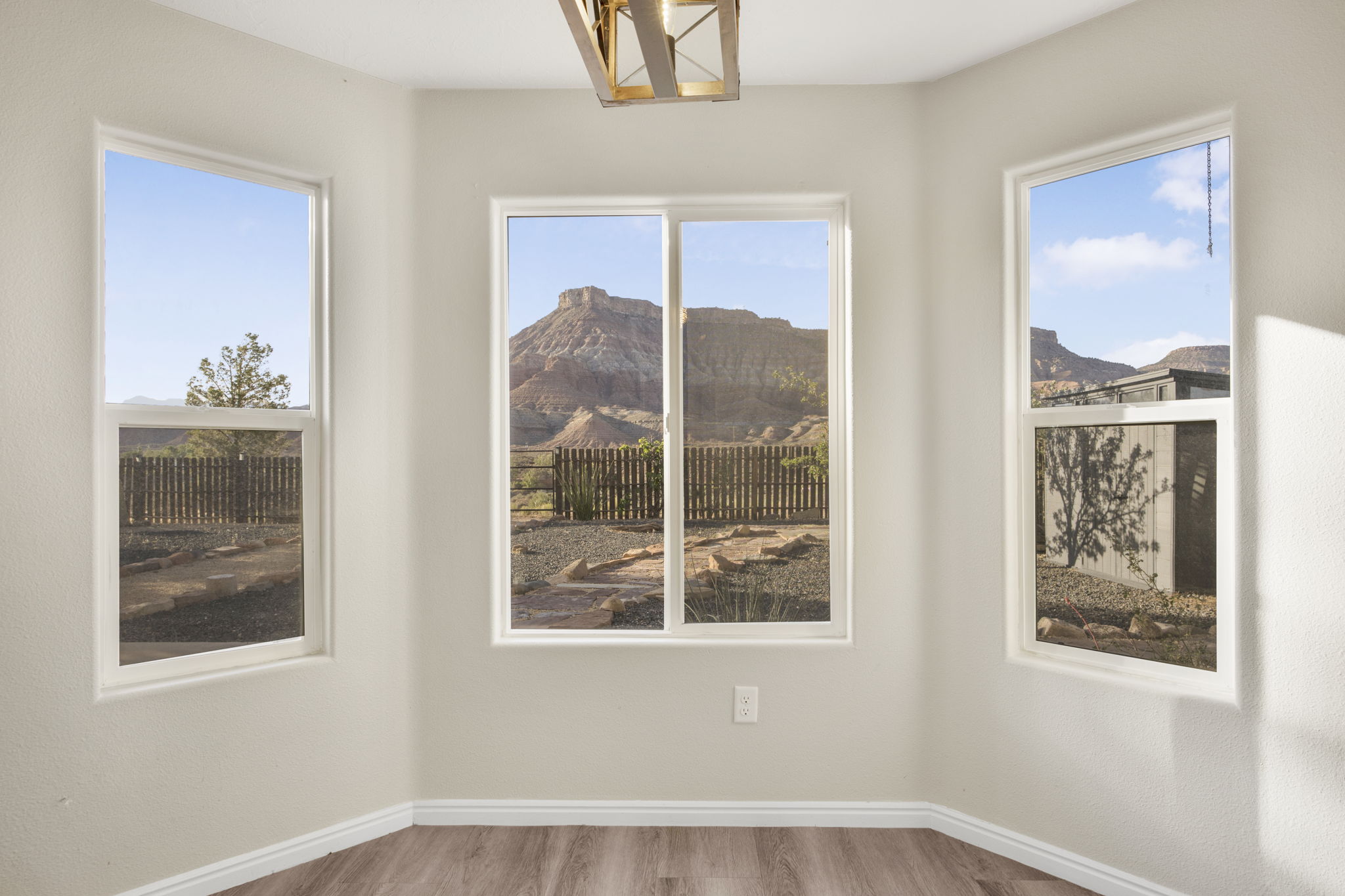 Bay window area featuring three expansive windows, wood-finish flooring, white baseboards, and a contemporary ceiling light fixture