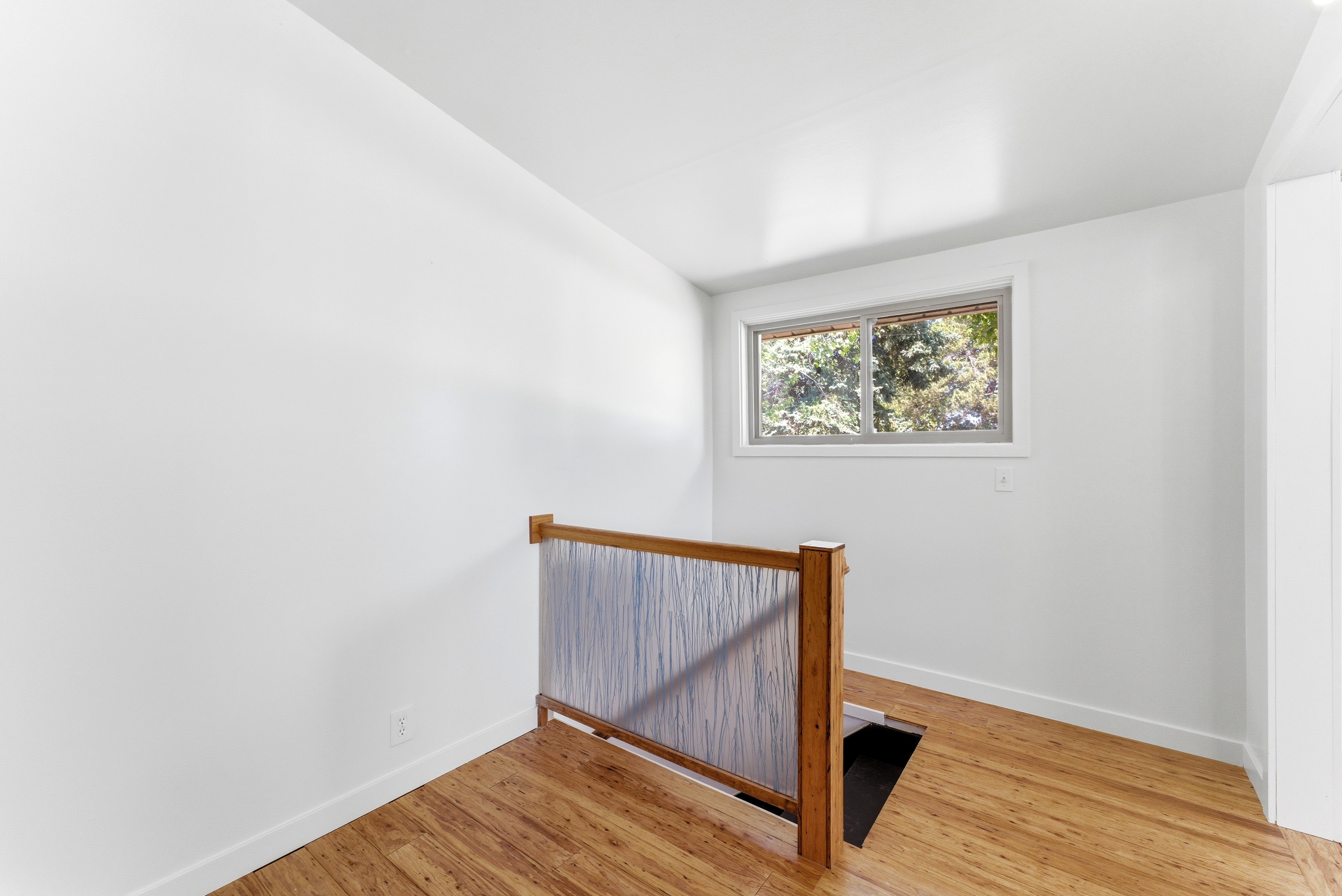 Upper-level landing featuring wood-finish flooring, a contemporary railing with wooden posts and a textured panel, a double-pane window, and a bright white ceiling