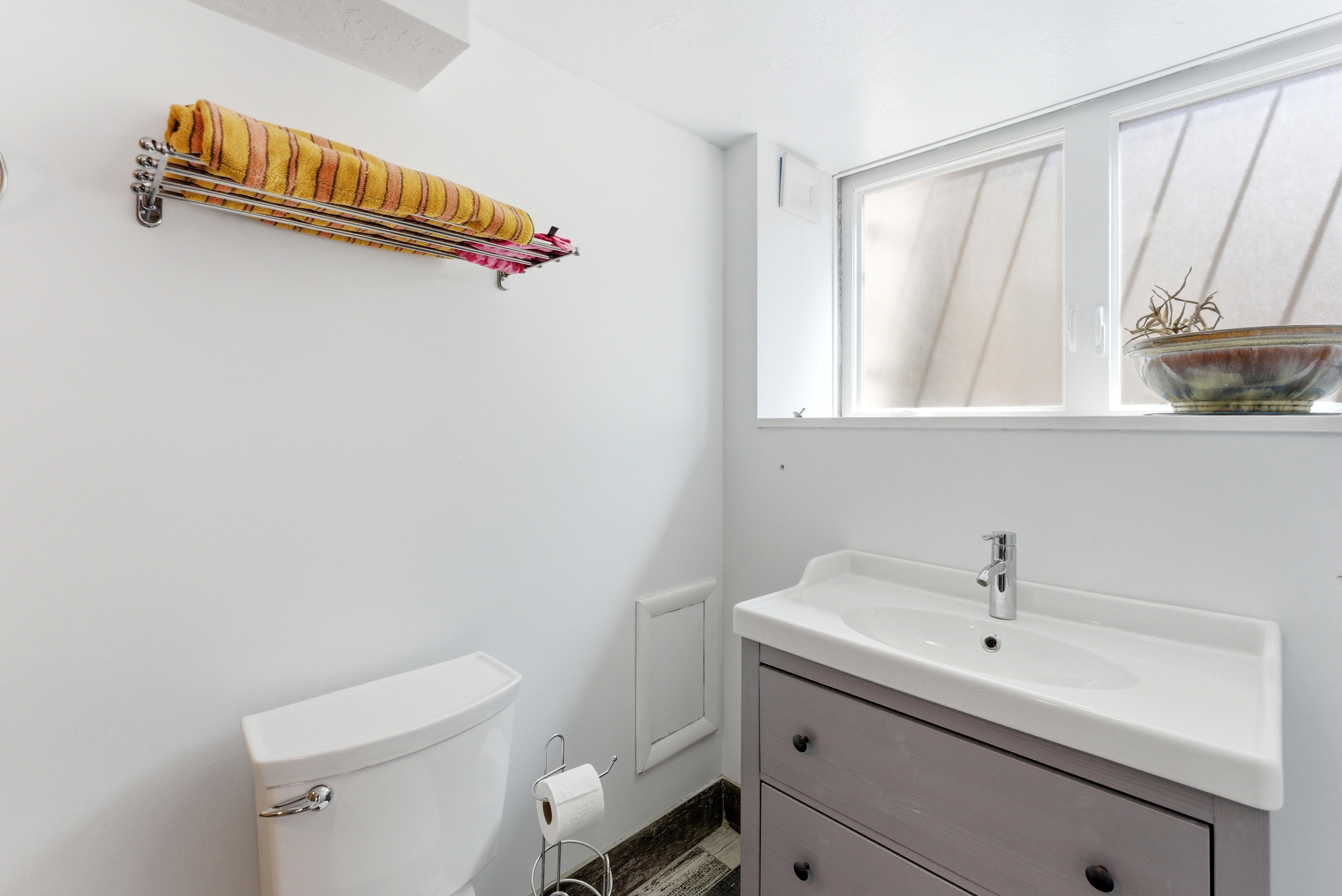 Bathroom featuring a white toilet, a vanity with a white countertop and basin, and a gray cabinet with black drawer pulls
