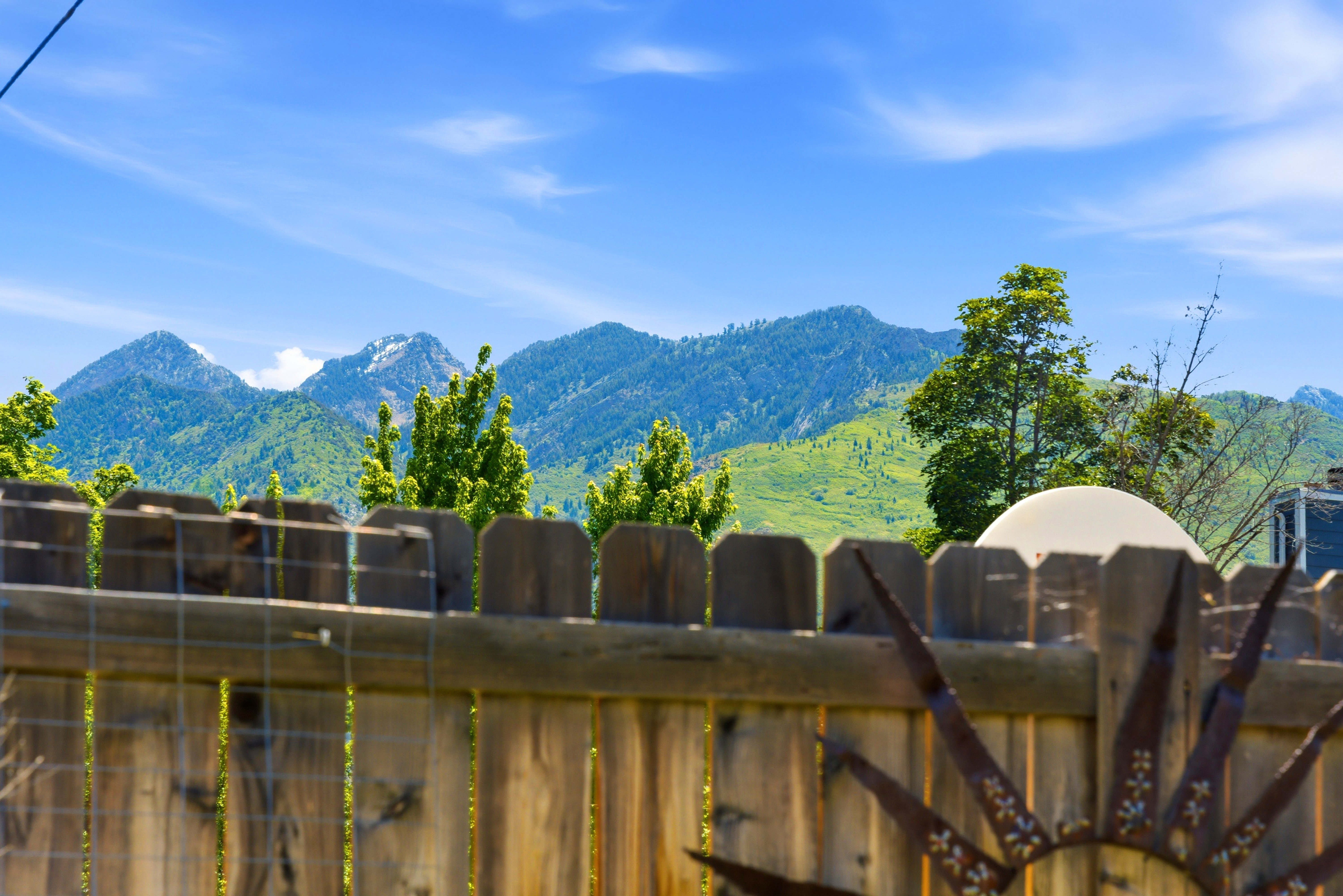 Wood privacy fence with an ornamental sunburst accent, framing distant mountains under a blue sky