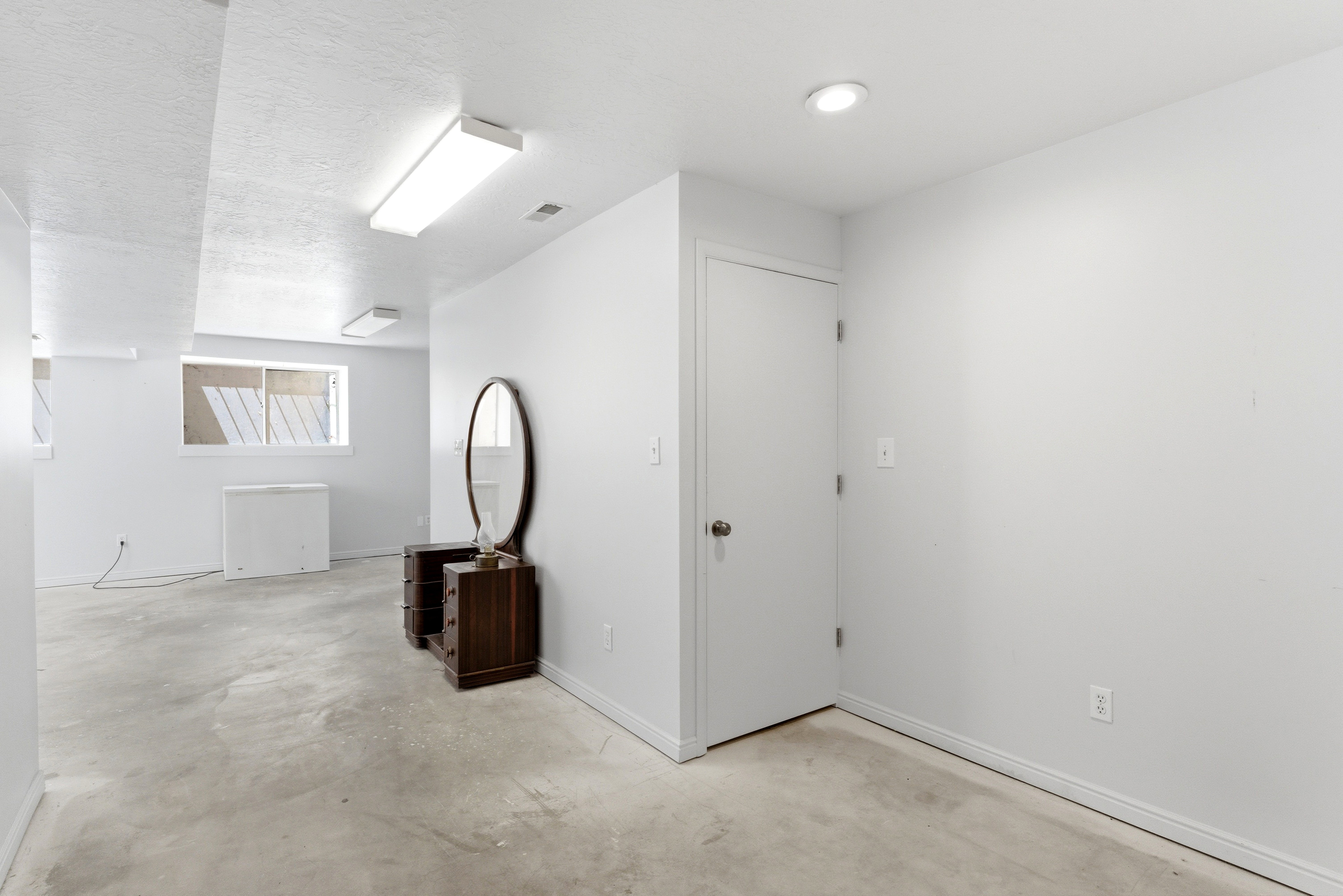 Spacious room featuring light gray concrete flooring, white painted walls, and a white ceiling