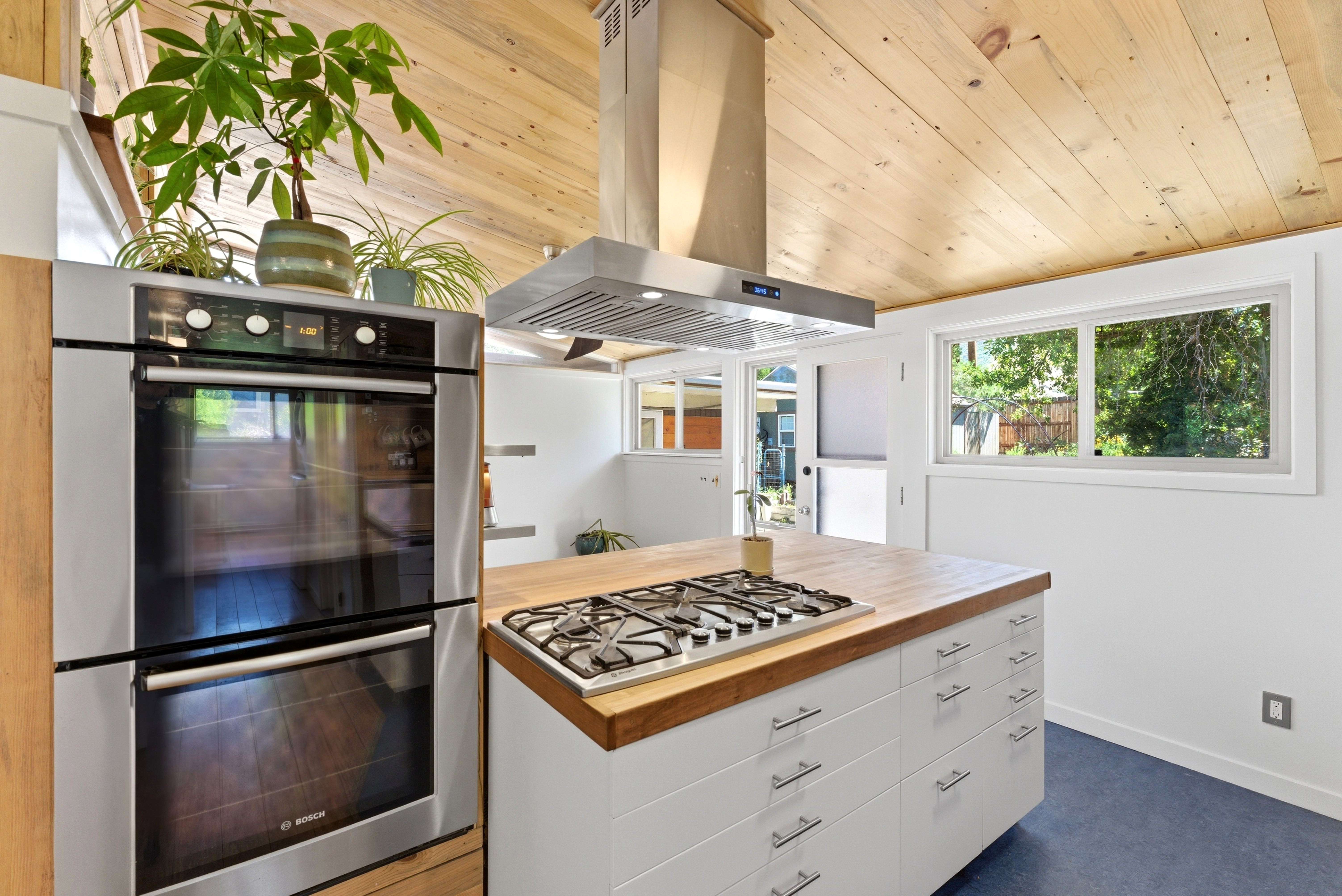 Kitchen featuring a central island with a gas cooktop and wood-finish countertop, stainless steel double wall oven, and a wood-paneled vaulted ceiling