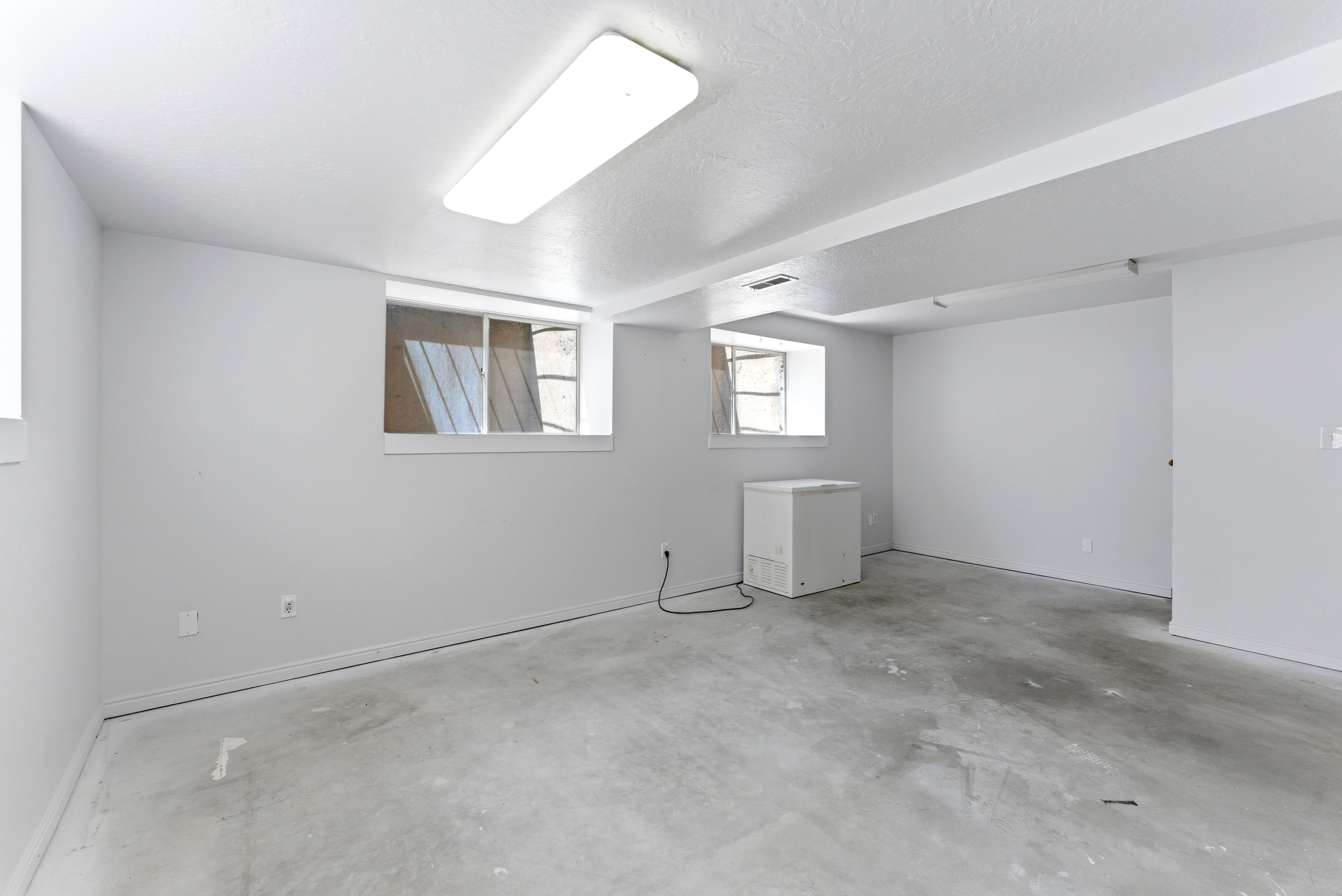 Spacious room featuring light gray walls, exposed concrete flooring, and multiple high-set windows
