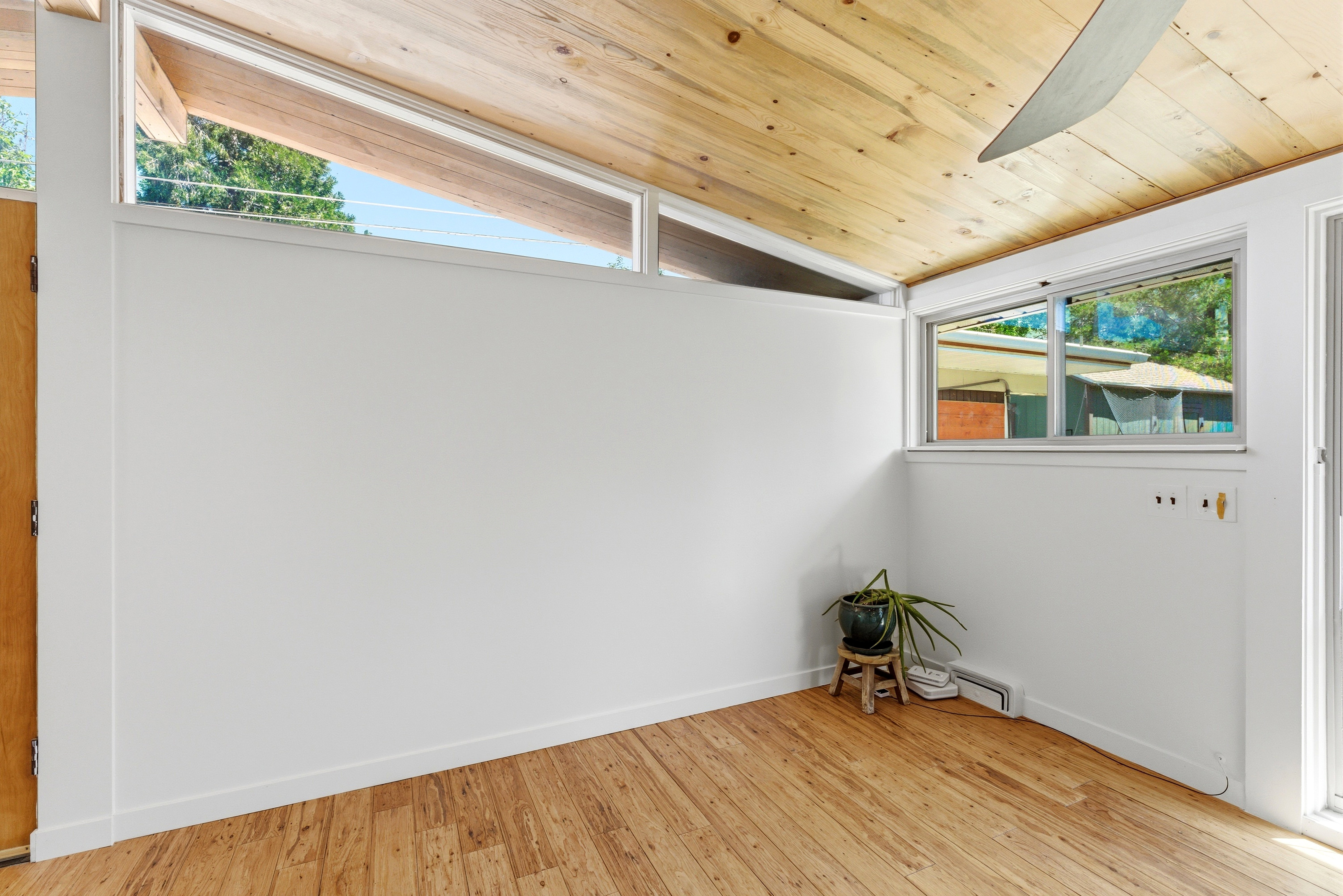 Slanted wood-finish ceiling with a ceiling fan, clerestory windows, wood-finish flooring, and white painted walls