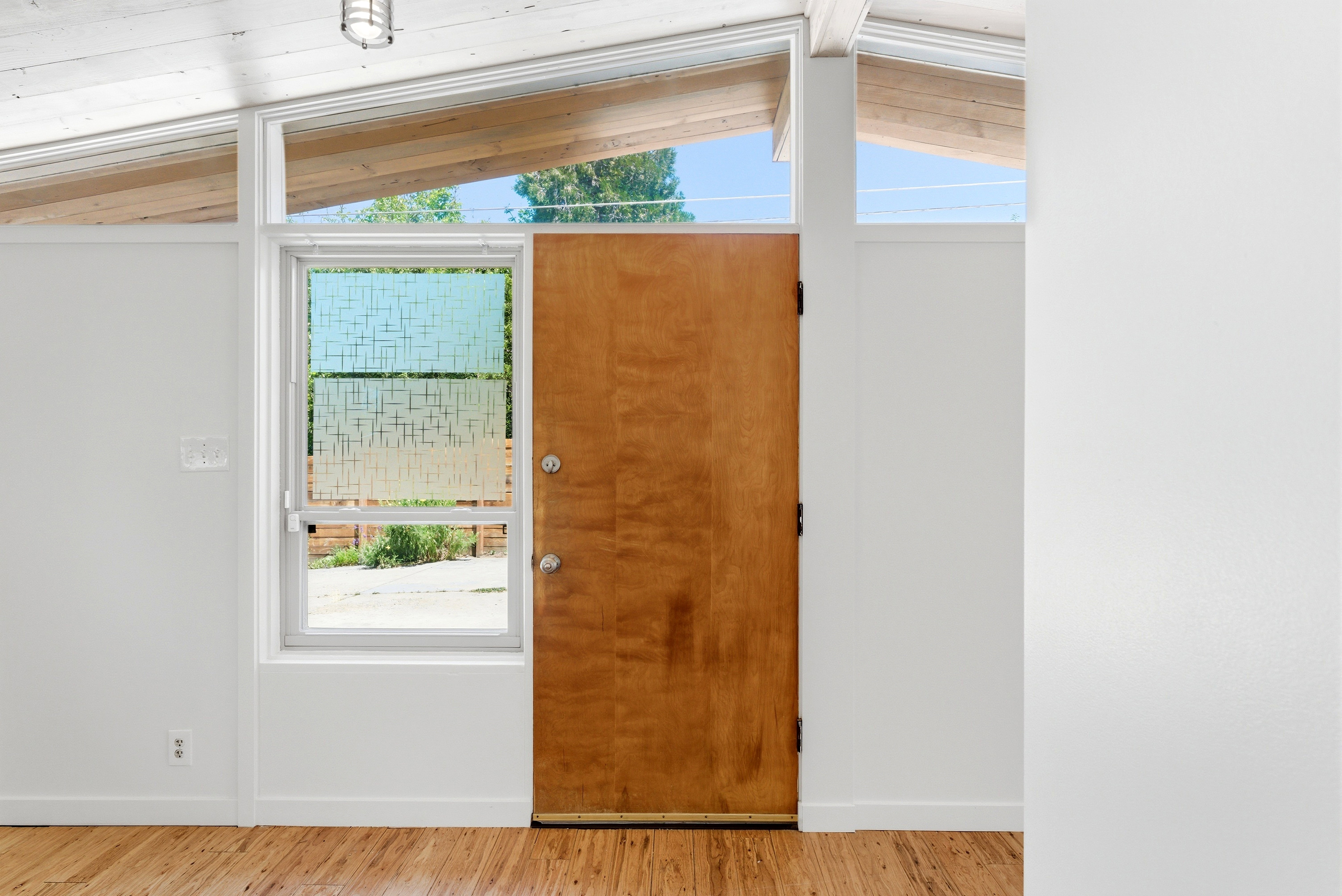 Entryway featuring a natural wood door, a window with decorative privacy film, and clerestory windows