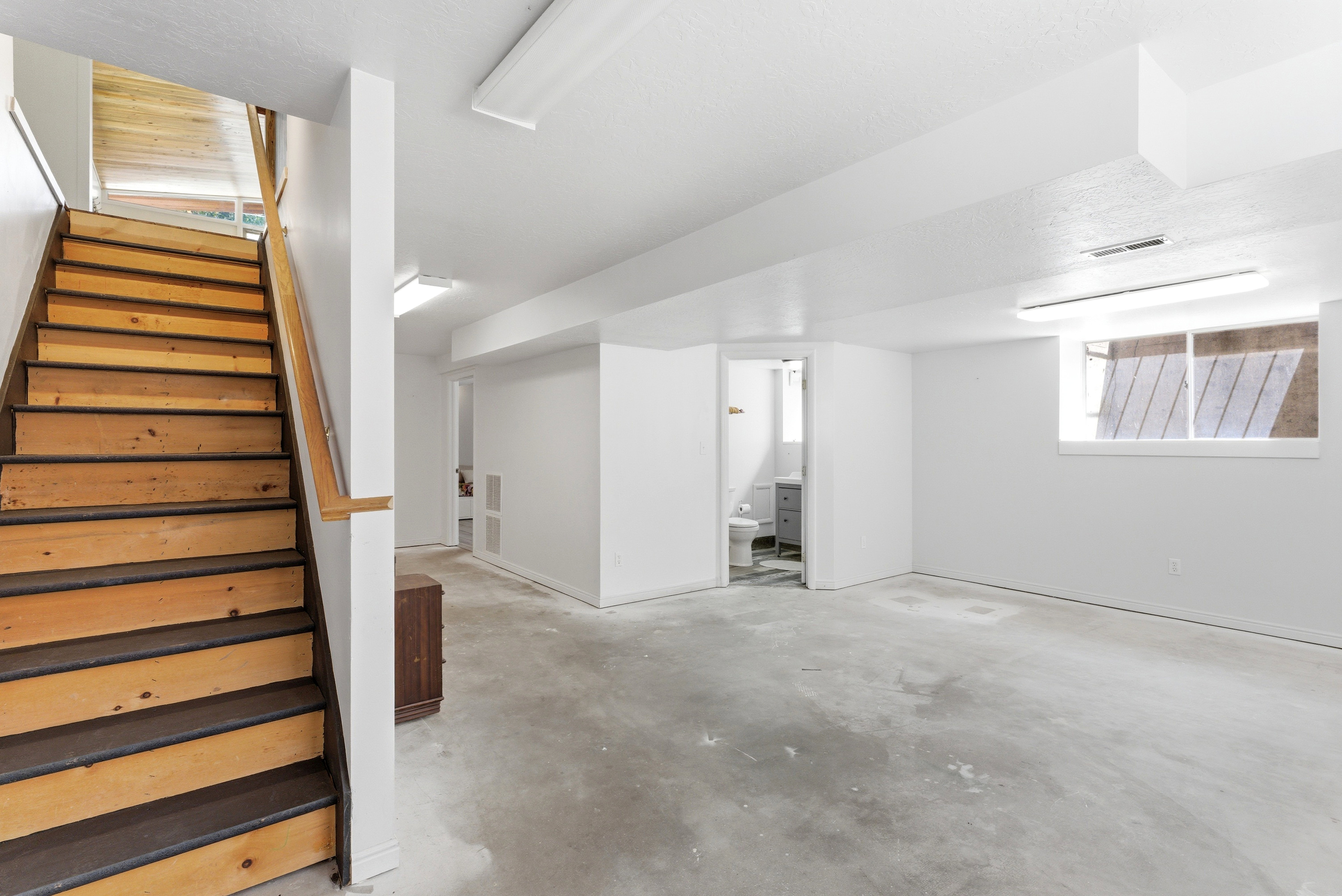 Open basement area featuring concrete flooring, white painted walls, and overhead fluorescent lighting