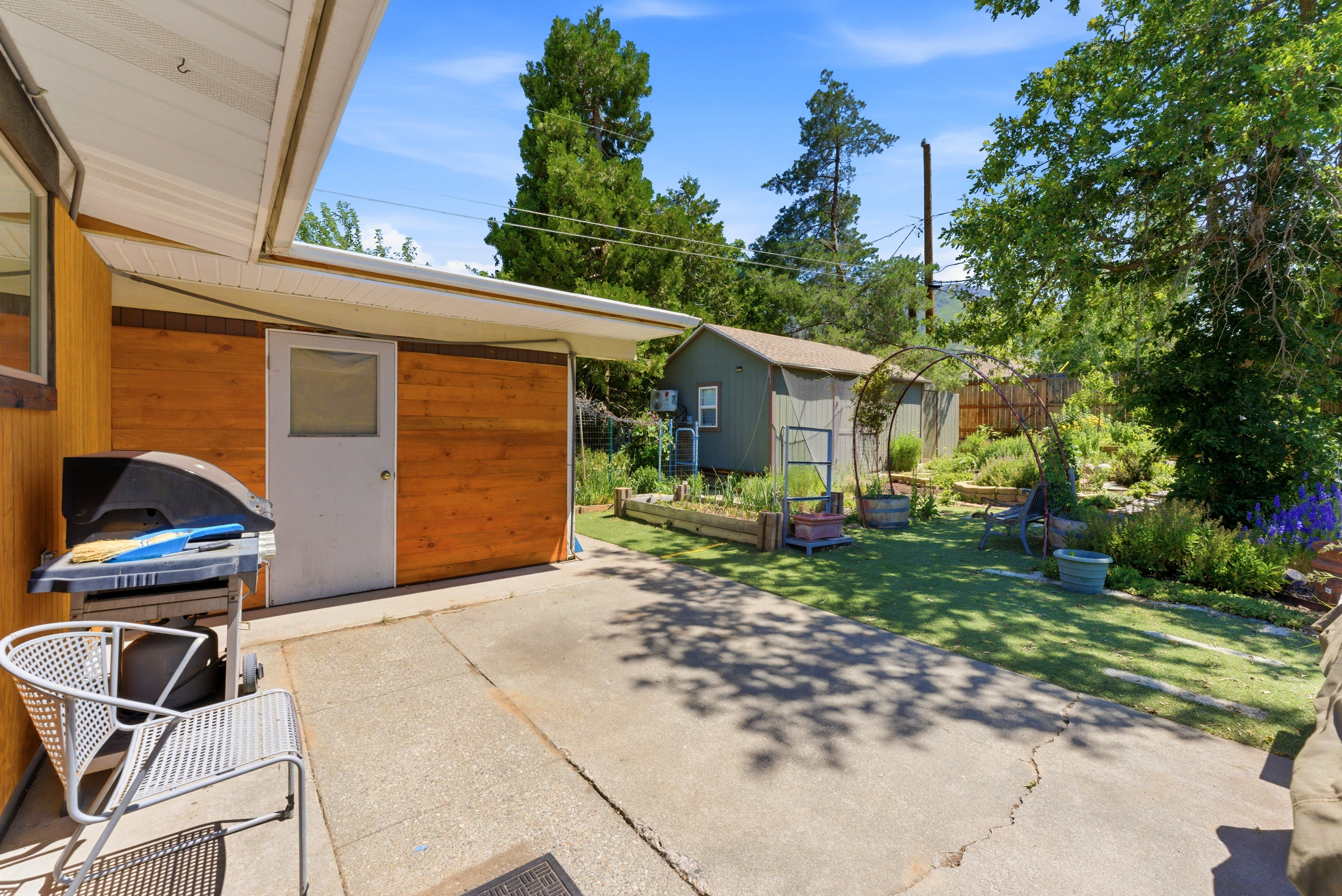 Paved patio space featuring a covered entryway with a private door, wood-paneled exterior walls, and a manicured lawn area